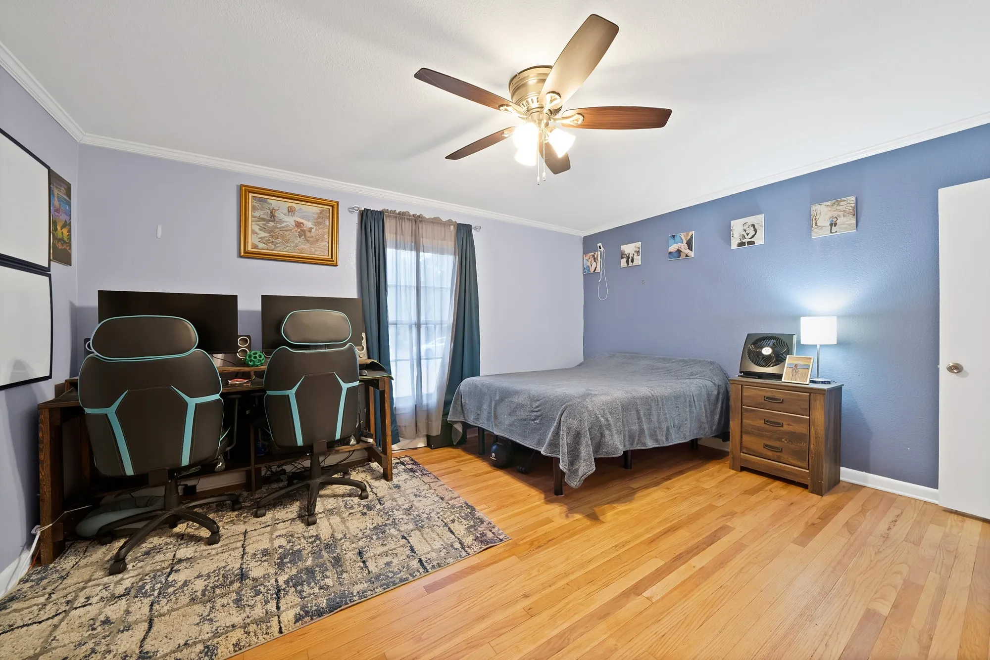 Hardwood flooring throughout, featuring a ceiling fan, a window with drapery, and a solid wood nightstand