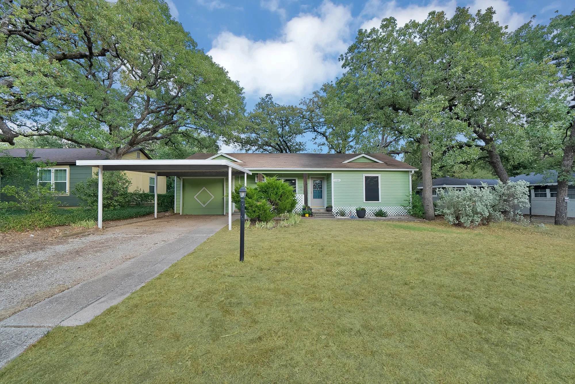 Expansive front lawn with mature trees, a covered carport, and a drive-through garage