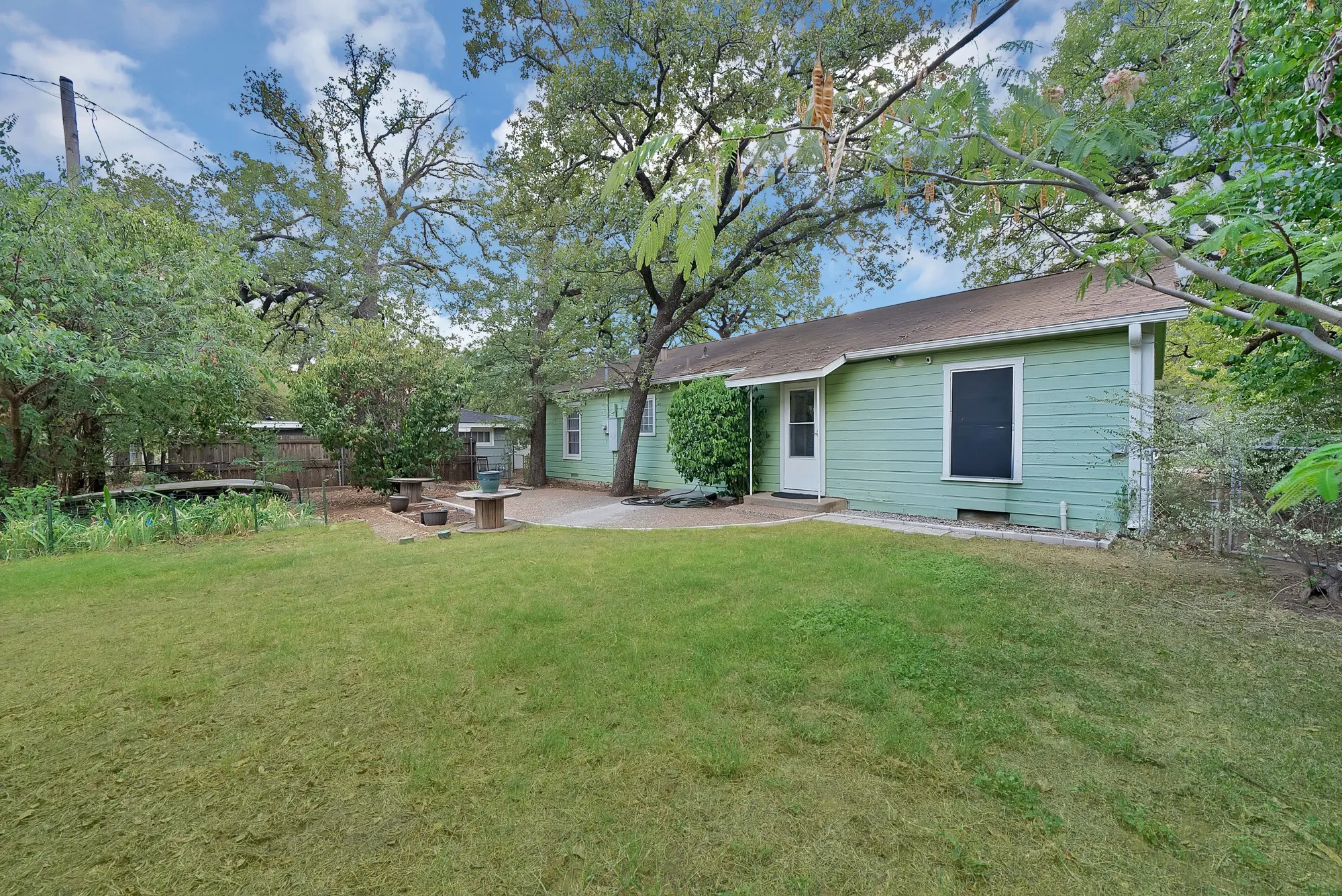 Expansive green lawn, mature trees, light green horizontal siding, and a paved patio area