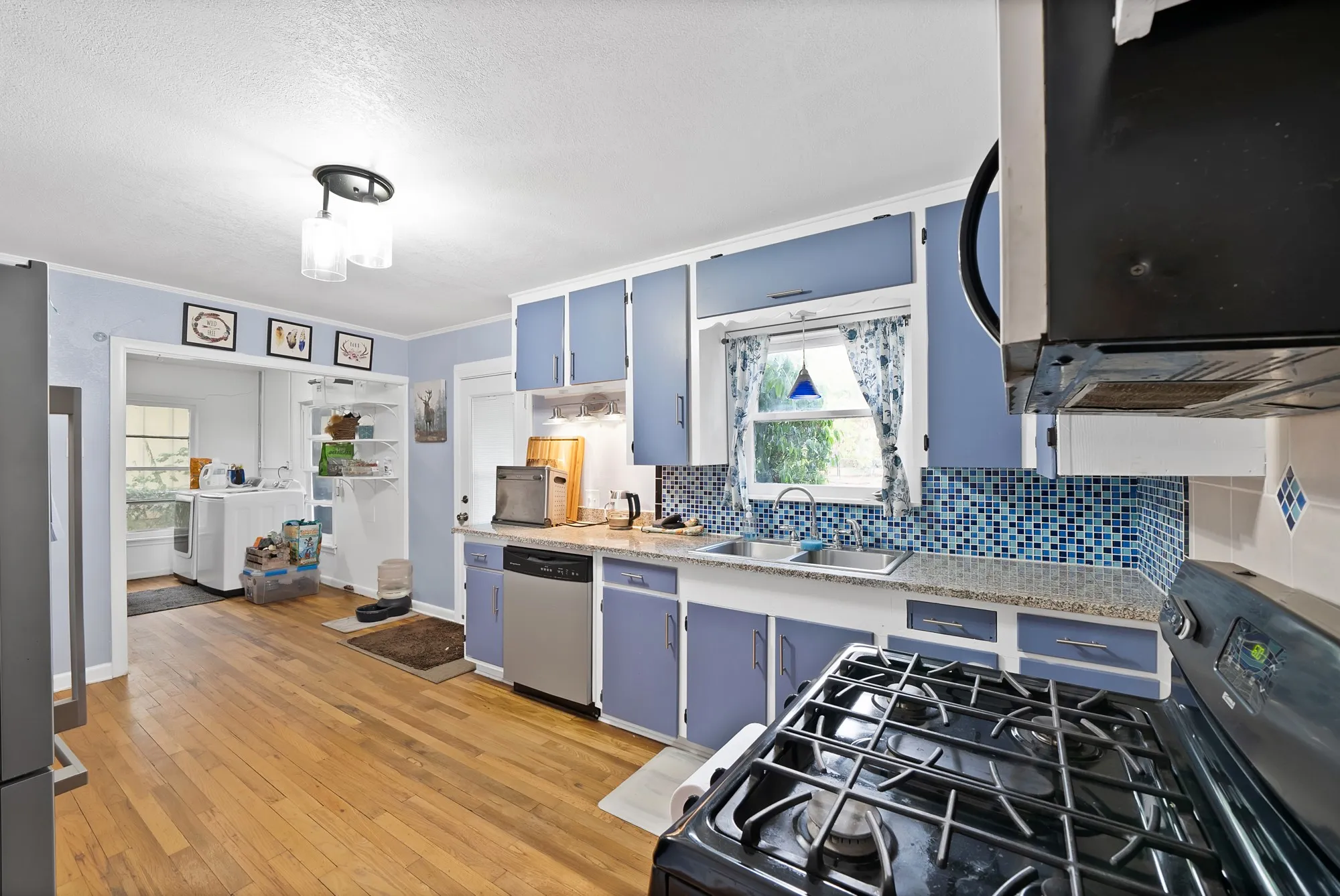 Kitchen featuring wood-finish flooring, blue cabinetry, granite-style countertops, and a mosaic tile backsplash