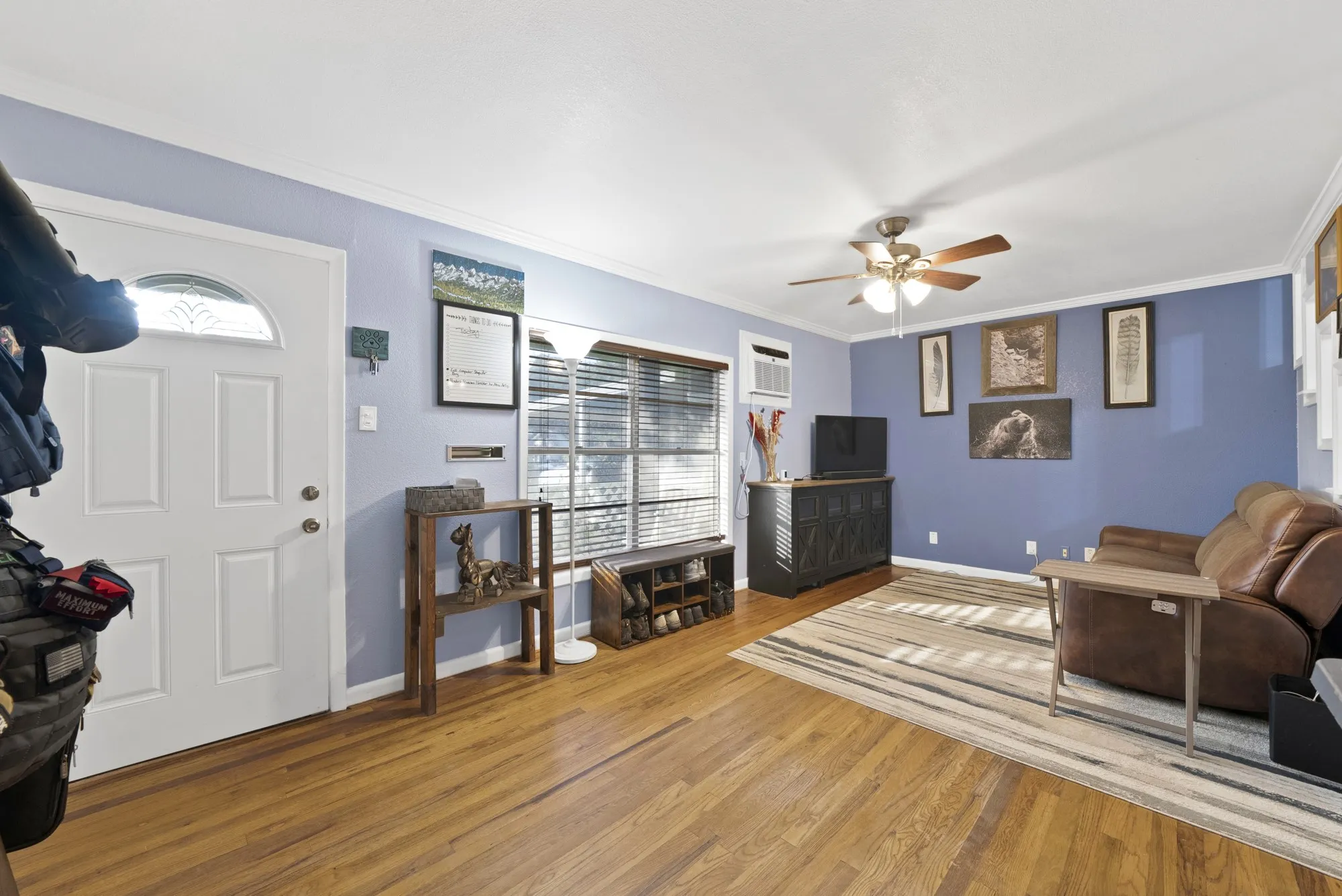 Wood-finish flooring throughout, ceiling fan with integrated lighting, and multiple windows with blinds