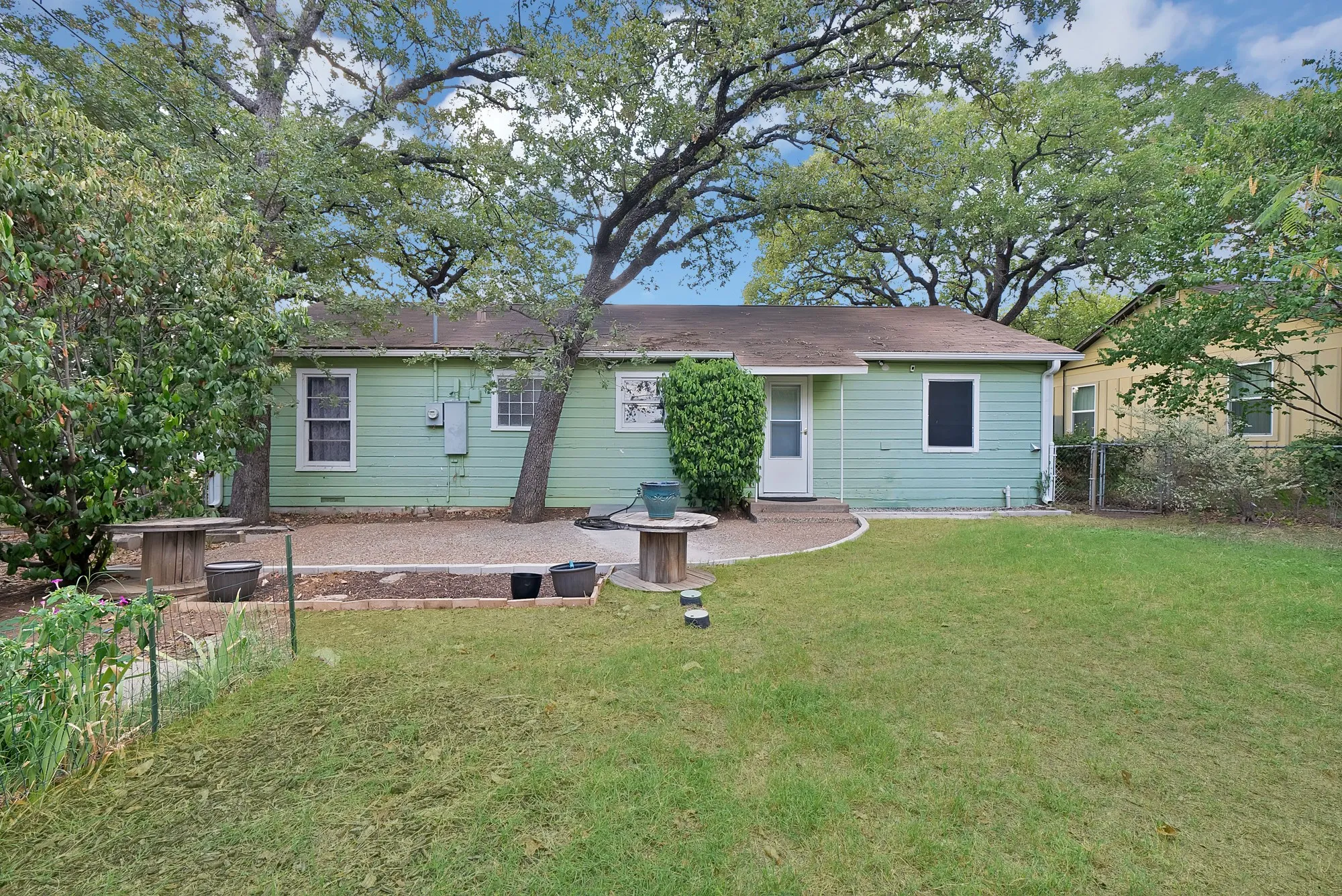 Expansive backyard featuring a green lawn, mature trees, and a gravel patio area