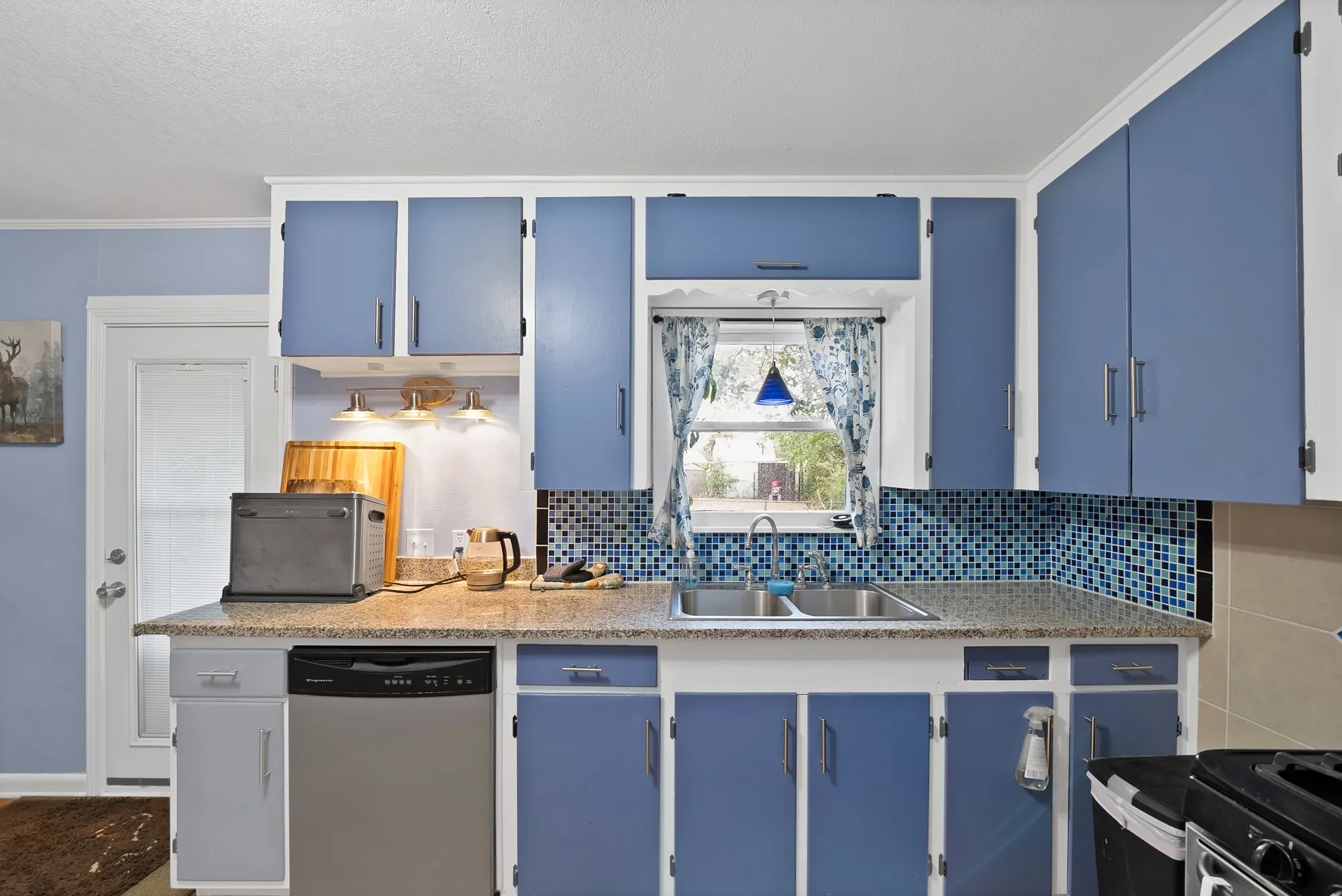 Kitchen featuring blue cabinetry, a stainless steel dishwasher, a dual basin sink, and a tiled backsplash