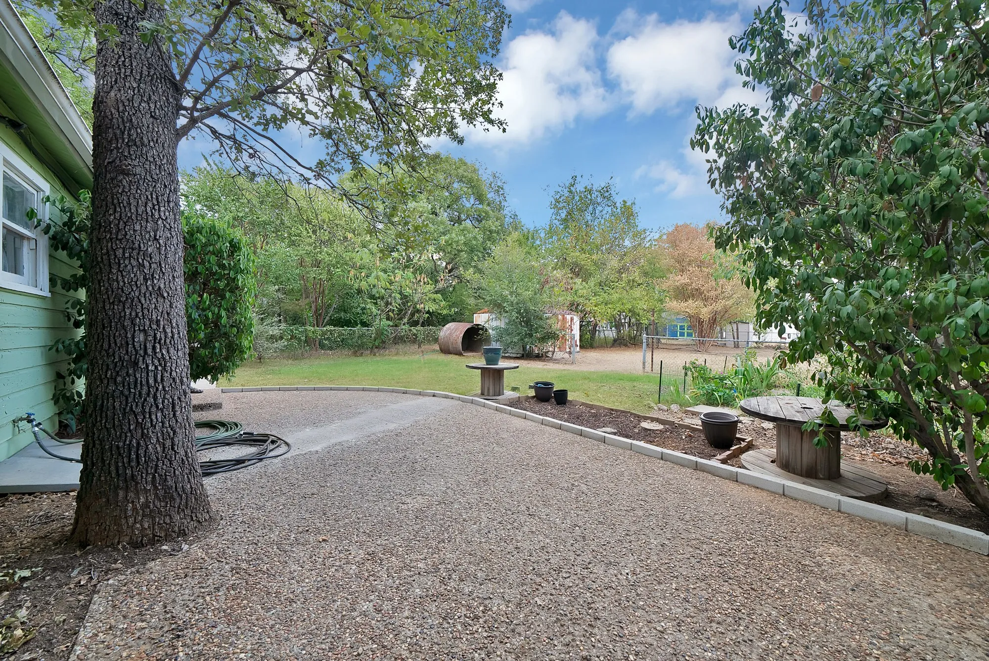 Gravel pathway leading to a expansive lawn area, bordered by mature trees and shrubs