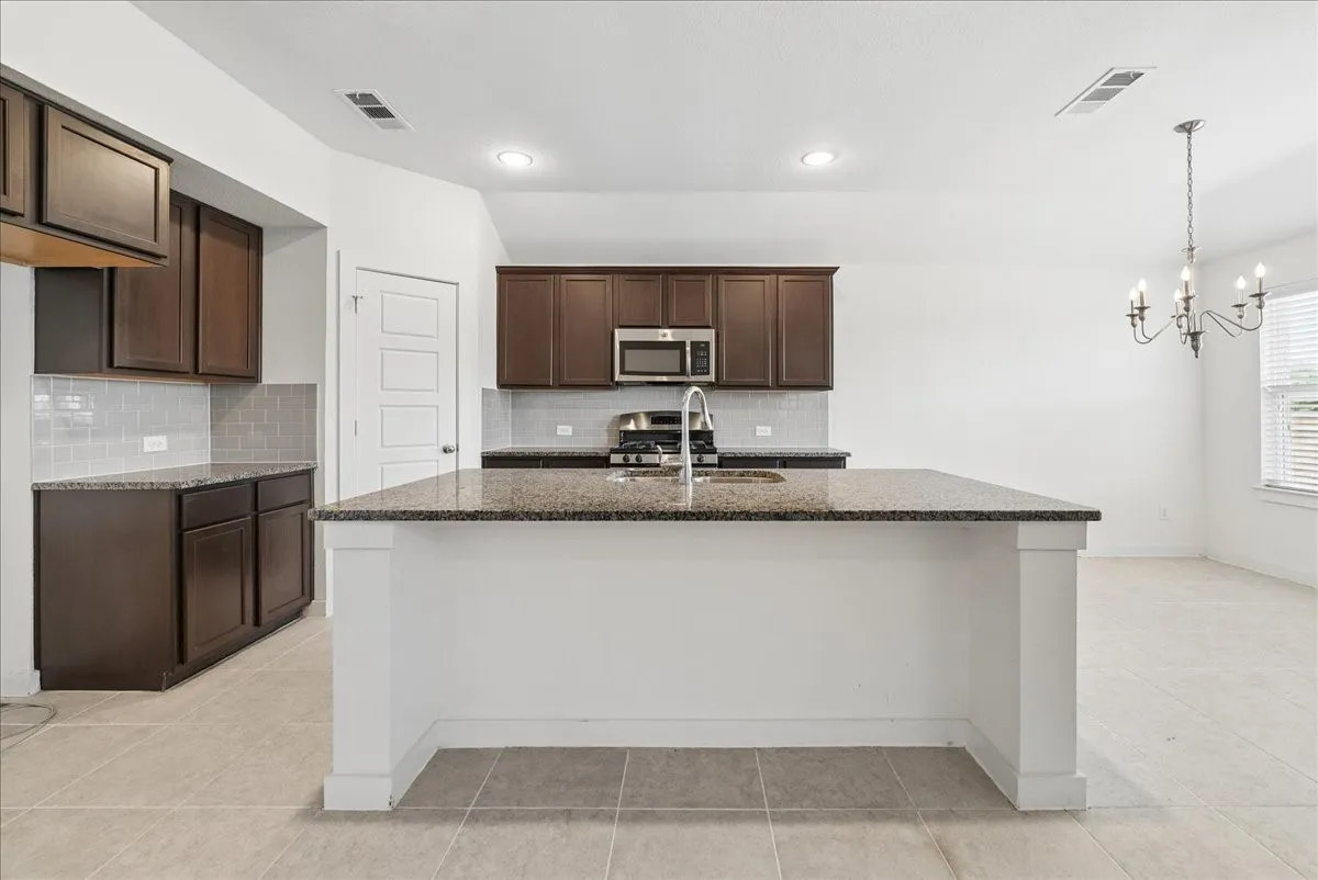 Kitchen featuring an island with granite countertops, dark wood-finish cabinetry, tile backsplash, and stainless steel appliances