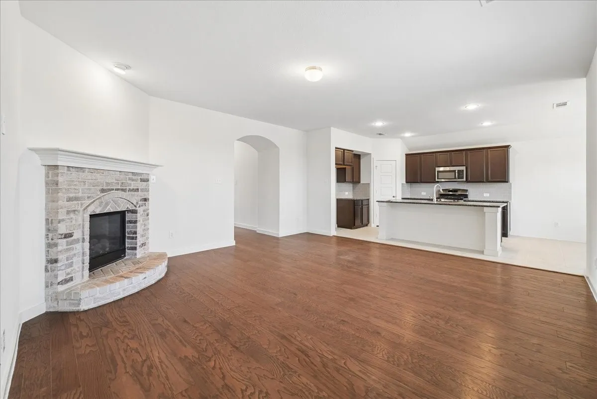 Wood-finish flooring, brick-surround fireplace with hearth, arched doorway, recessed lighting, and kitchen island with built-in sink