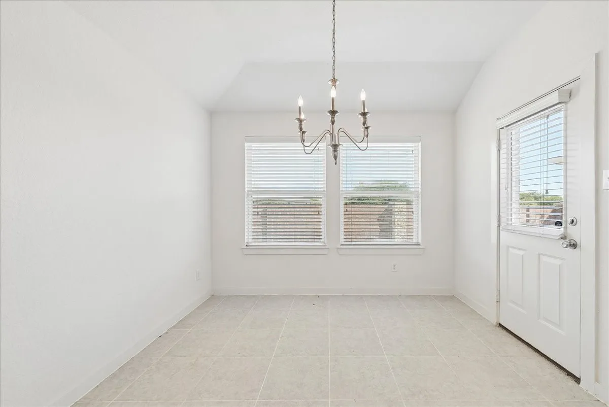 Recessed ceiling with an overhead chandelier, two windows with blinds, a white door with a window and blinds, and tiled flooring