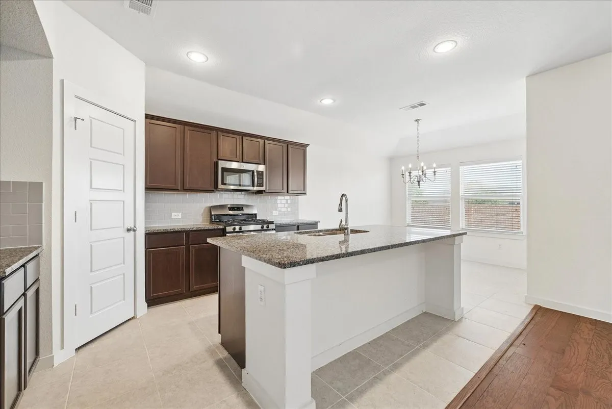 Kitchen featuring a large island with a stone-finish countertop, dark wood-finish cabinetry, stainless steel appliances, and recessed lighting