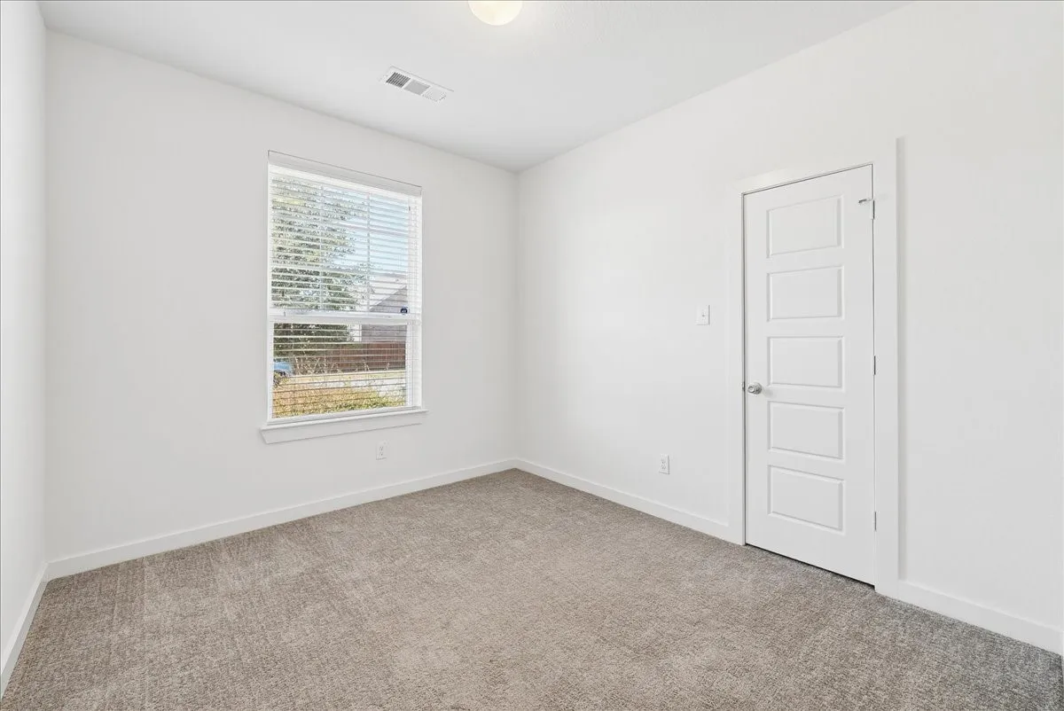 Neutral-toned carpet flooring, a multi-paneled interior door, and a single window with blinds