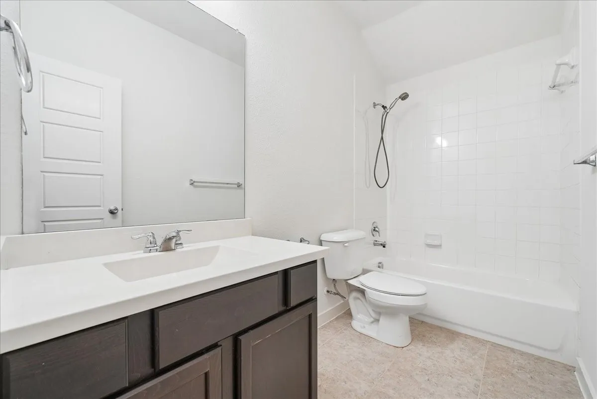 Vanity with an integrated sink and brushed nickel faucet, a large wall-mounted mirror, white subway tile shower surround, and tile flooring