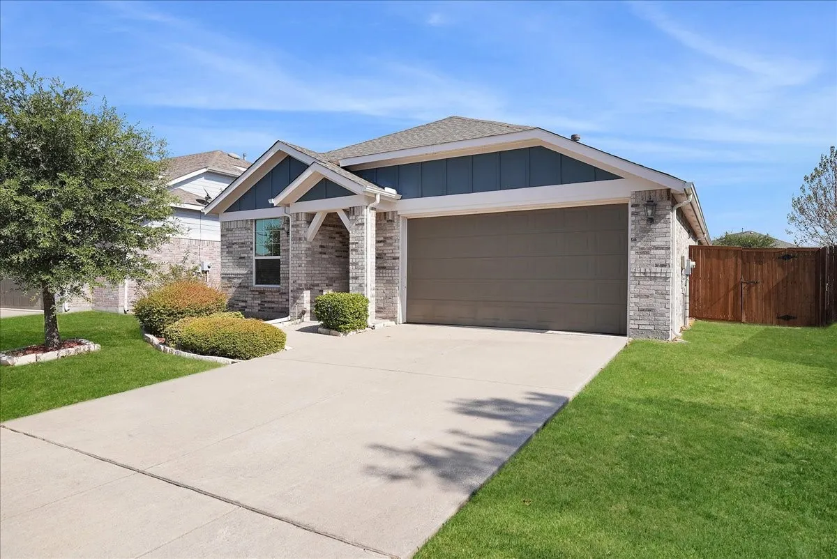 Brick veneer exterior with gabled roofline, concrete driveway, attached garage, and a wooden privacy fence