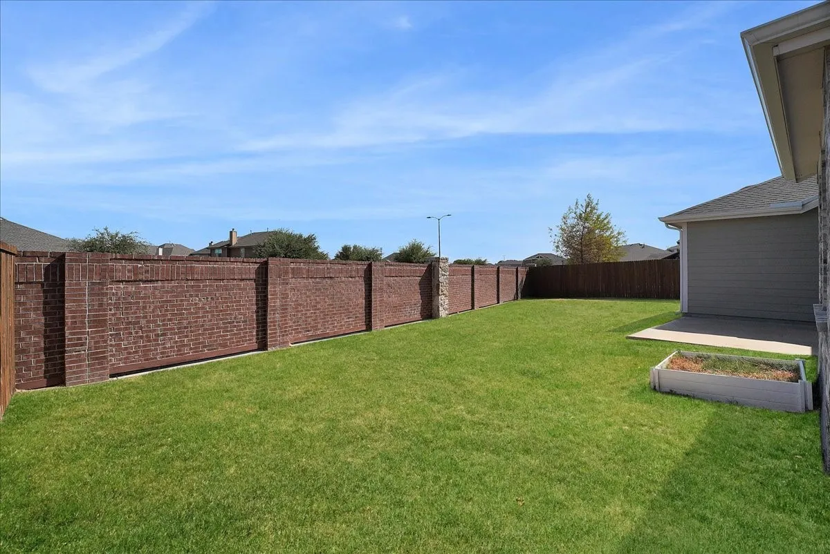 Expansive lawn area, brick and wood fencing, concrete patio, and a raised planter box