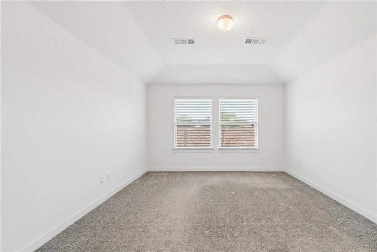 Vaulted ceiling with an attached light fixture, dual windows with blinds, light gray carpeting, and white baseboards
