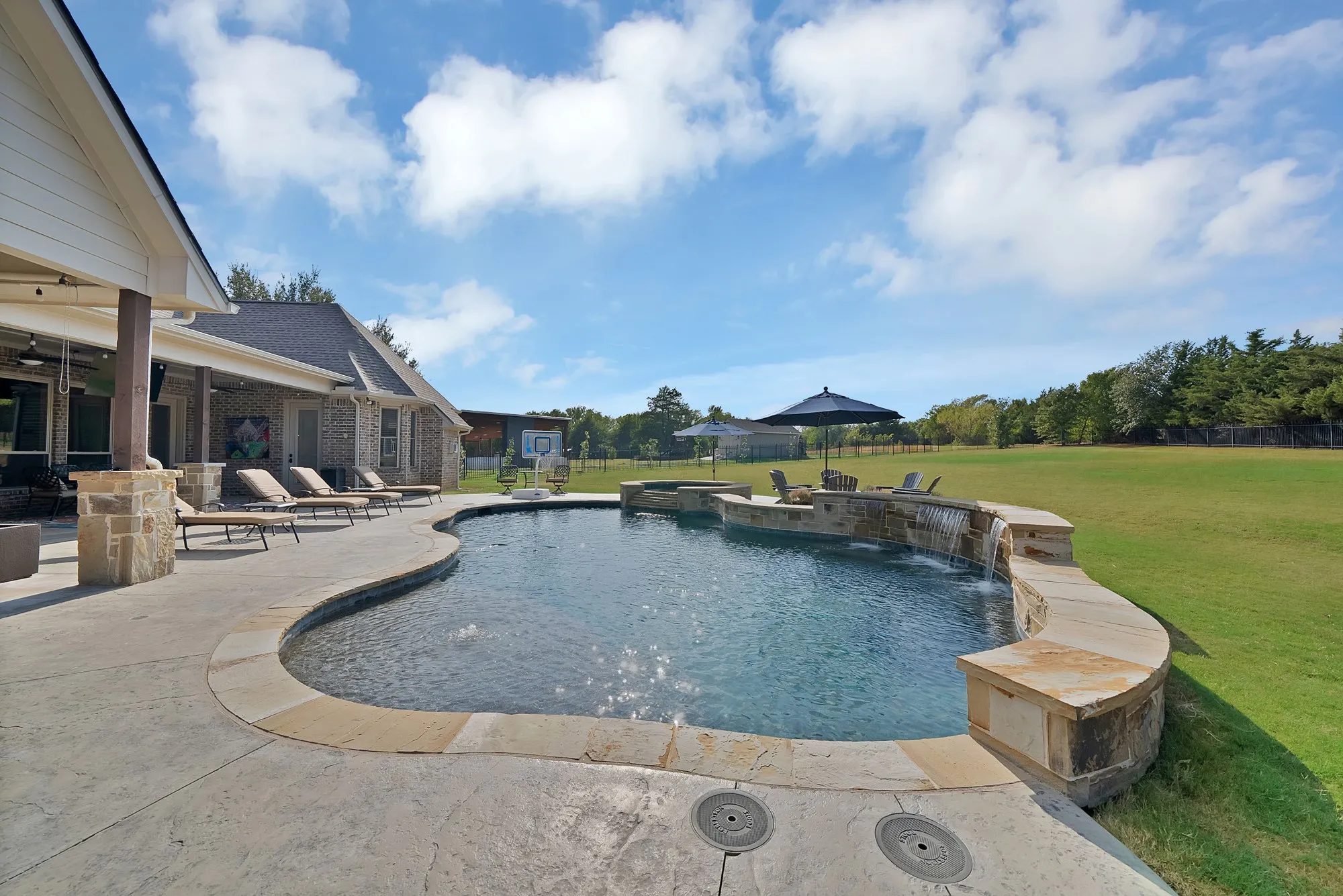 Expansive outdoor living area featuring a freeform swimming pool, integrated spa, and cascading water feature