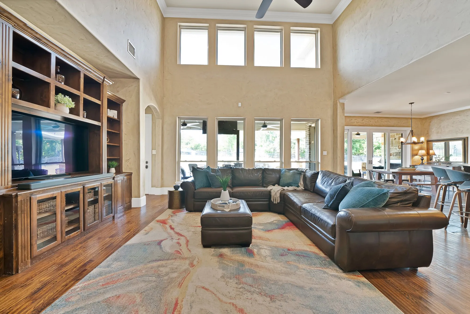 Vaulted ceiling with a ceiling fan, a built-in entertainment center with shelving, hand scraped hardwood floors, and multiple windows