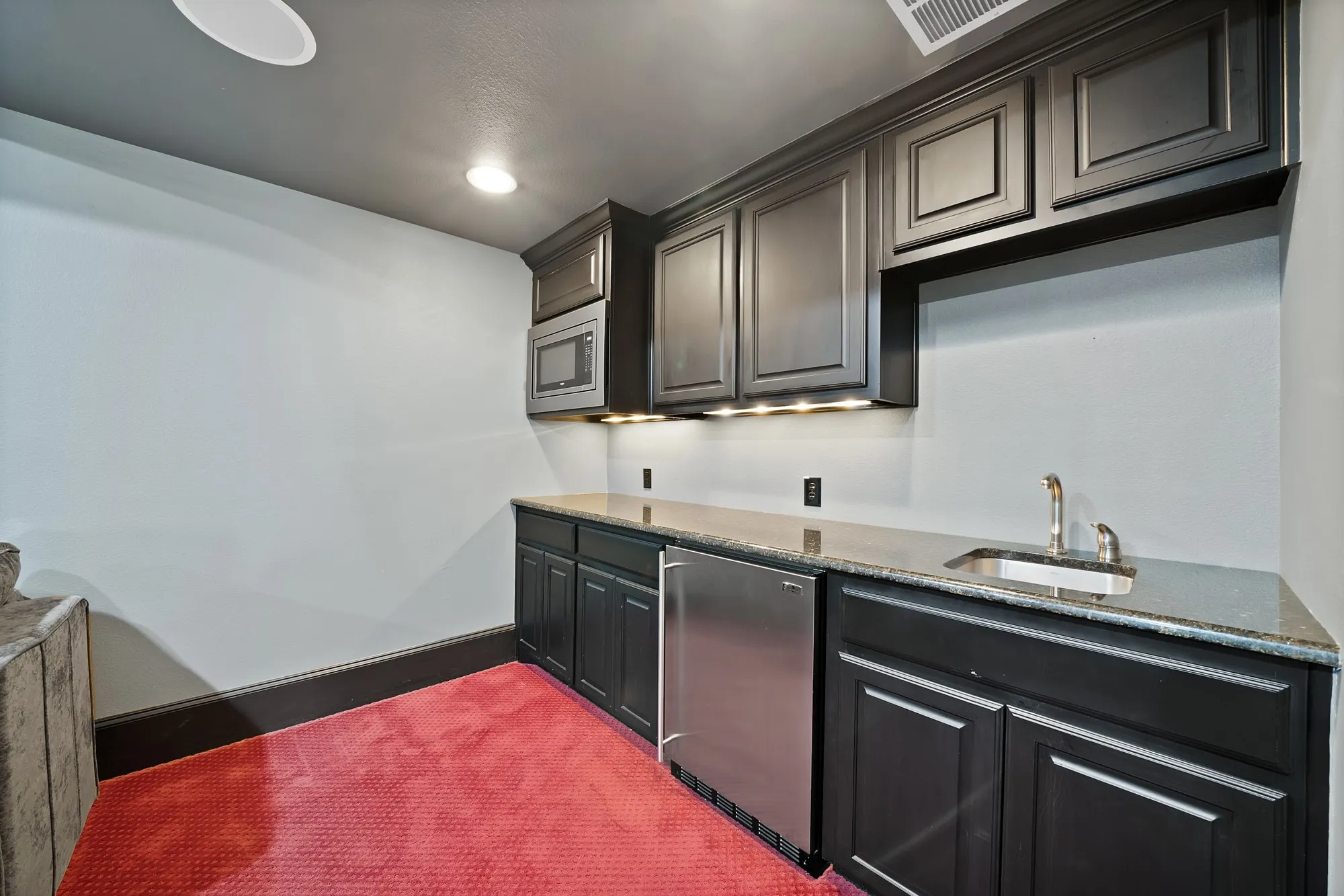 Built-in wet bar featuring dark cabinetry, stone countertops, undermount sink, stainless steel compact refrigerator, and under-cabinet lighting
