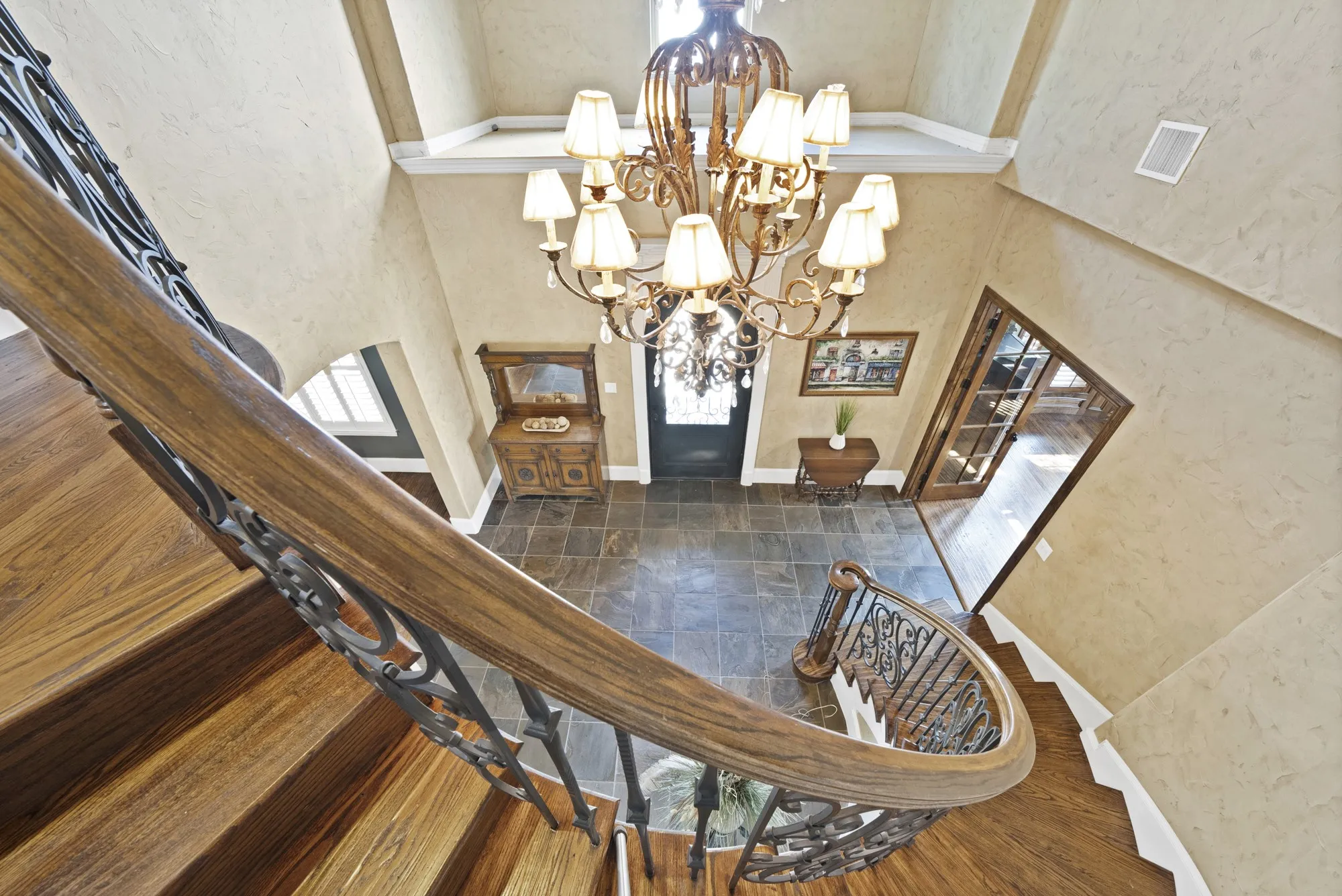 High ceilings with a decorative chandelier, tile flooring, hand scraped hardwood staircase with wrought iron balusters, and an arched entryway