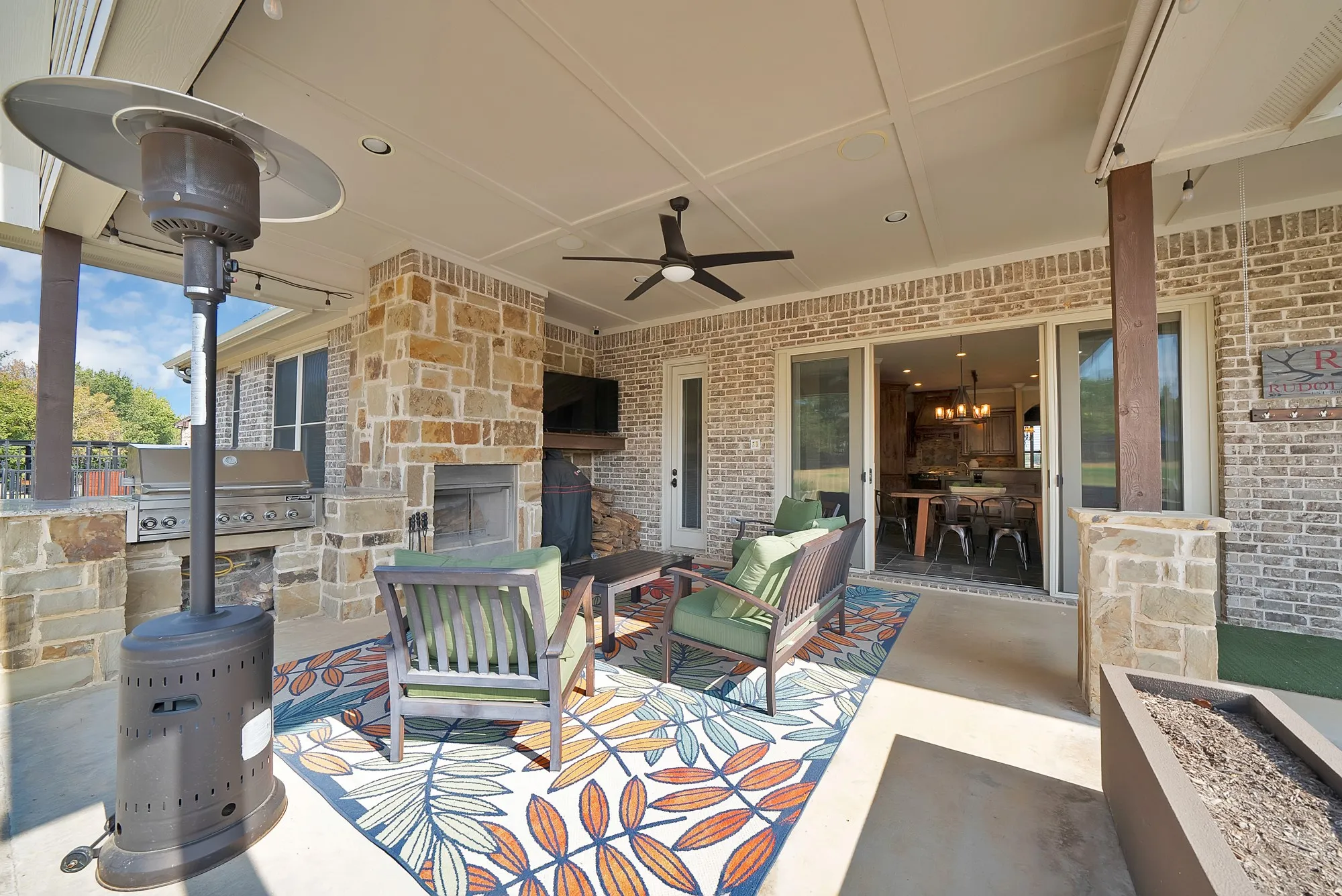 Covered patio featuring a stone fireplace, built-in outdoor grill, ceiling fan, and sliding glass doors