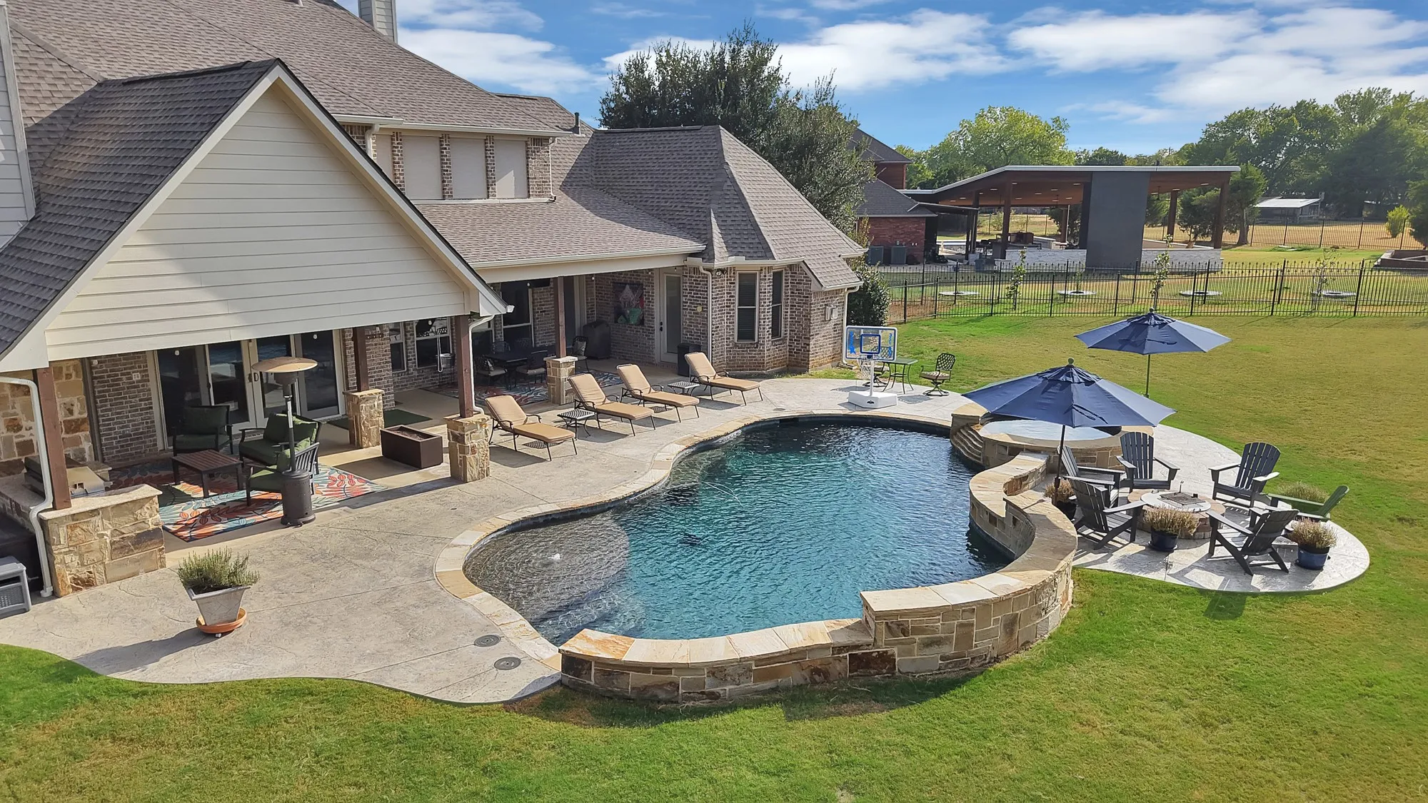 Resort-style backyard featuring a freeform swimming pool, integrated spa, and expansive patio with a built-in fire pit