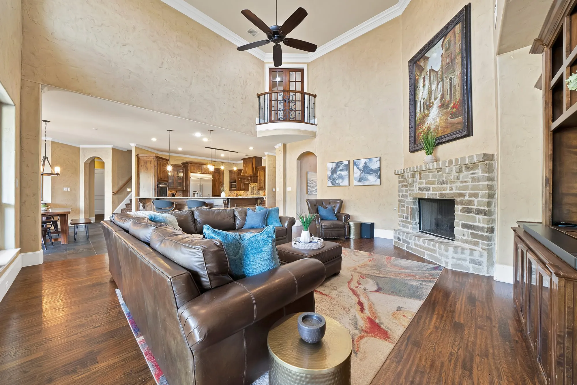 Expansive living area with high ceilings, a balcony overlook, a stone fireplace, hand scraped hardwood floors, and a ceiling fan