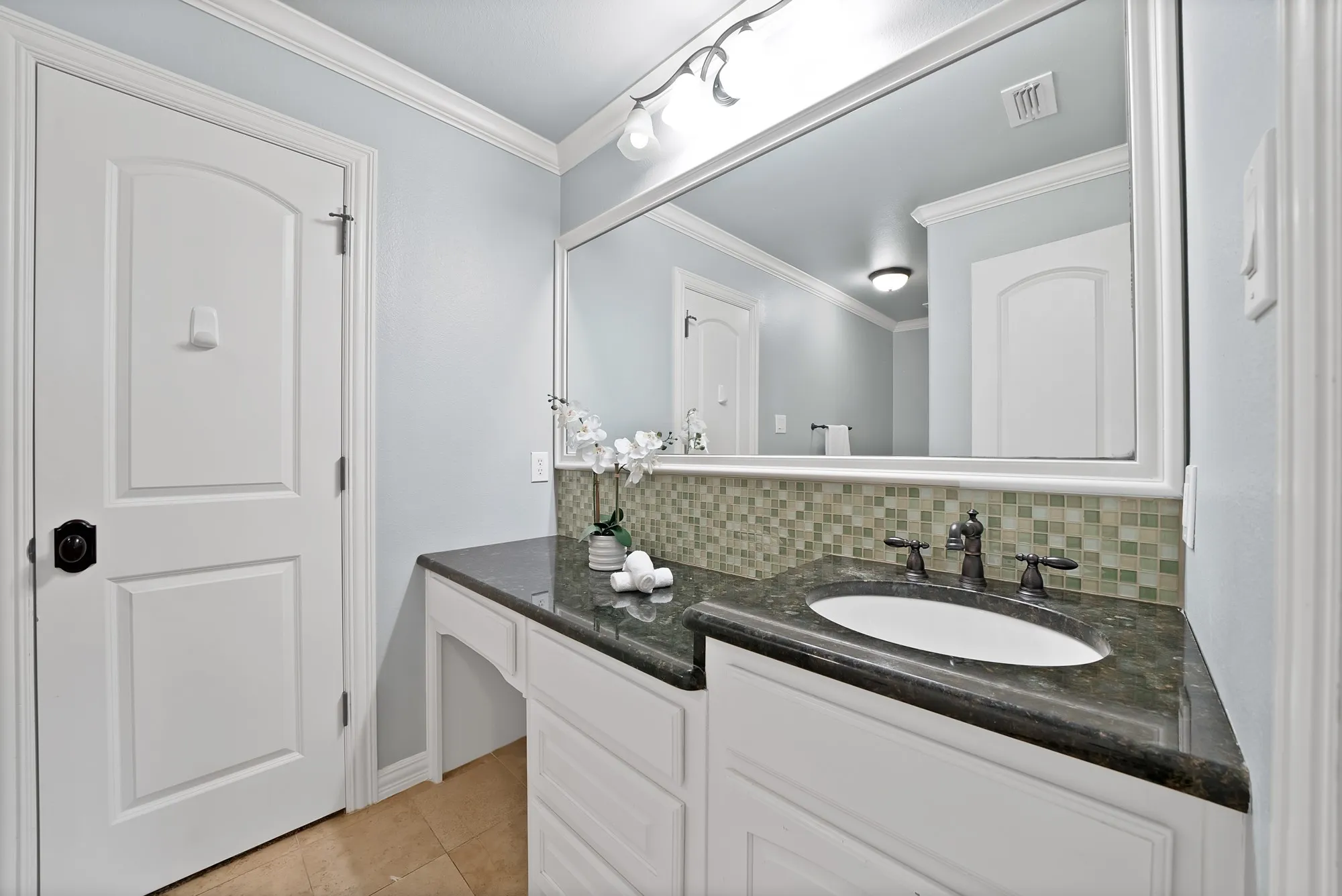 Spacious vanity with an integrated sink, dark countertop, and mosaic tile backsplash