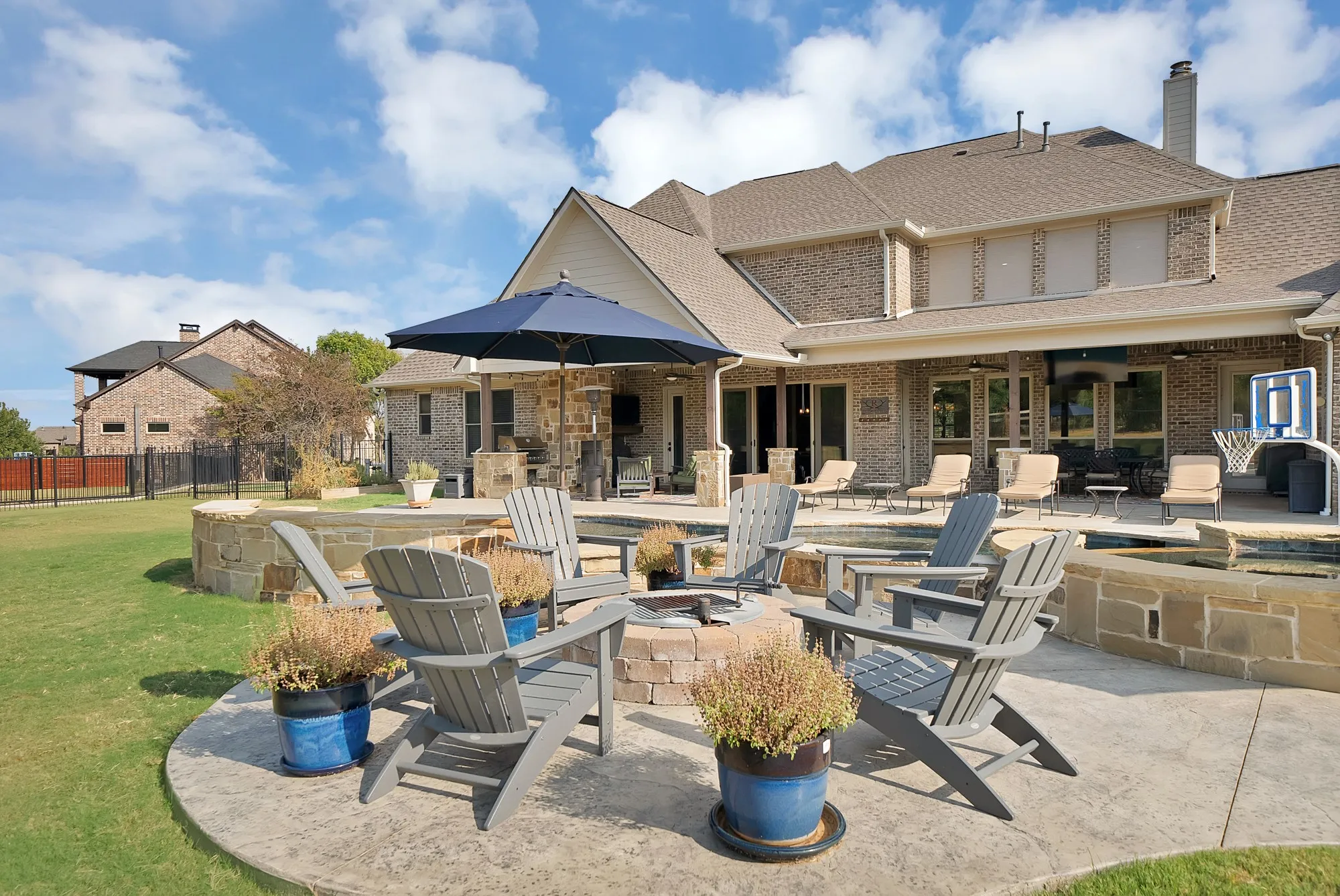 Expansive backyard featuring a stamped concrete patio, stone-clad fire pit, and a custom pool with stone coping