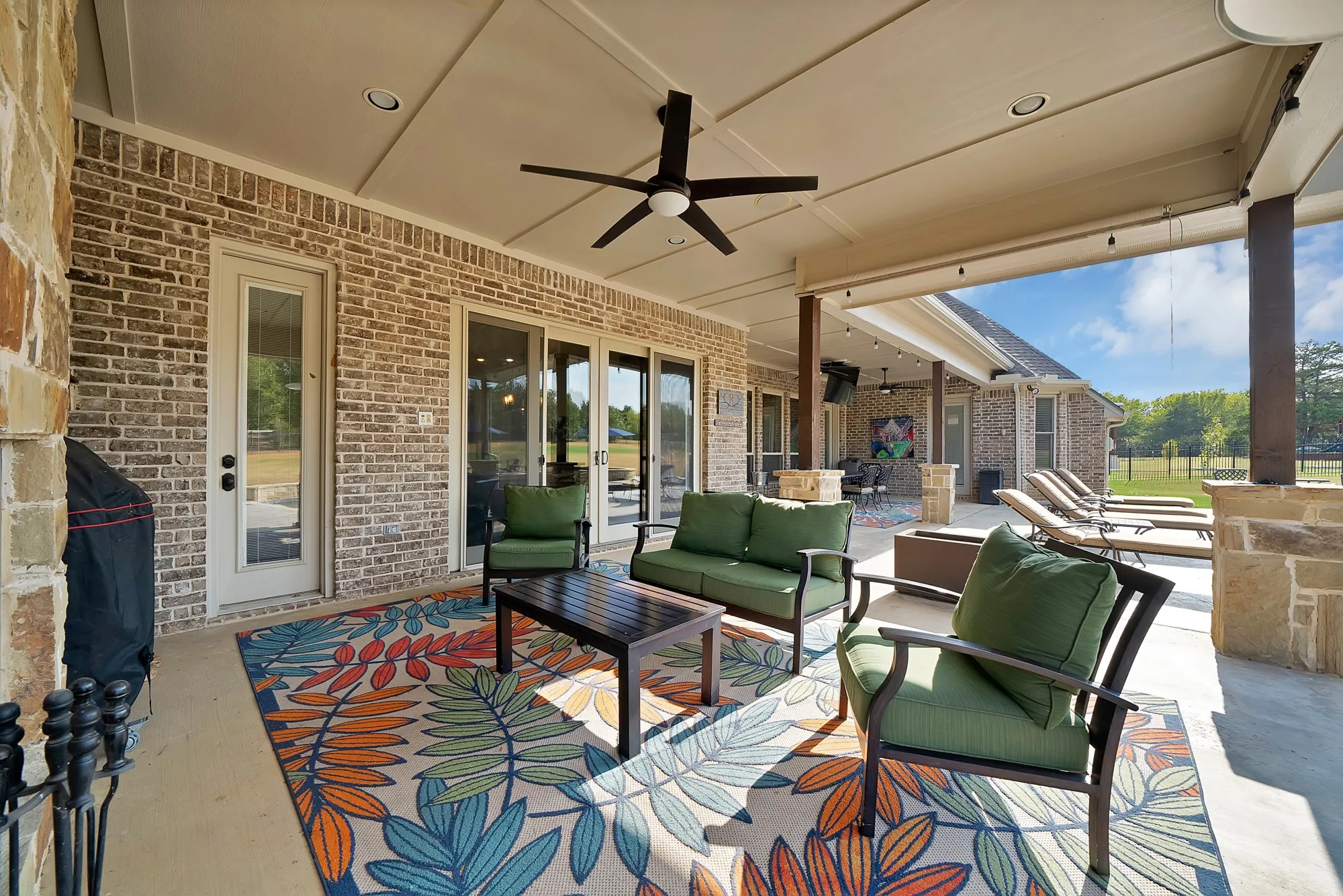 Expansive covered patio featuring brick and stone accent walls, recessed lighting, and a ceiling fan