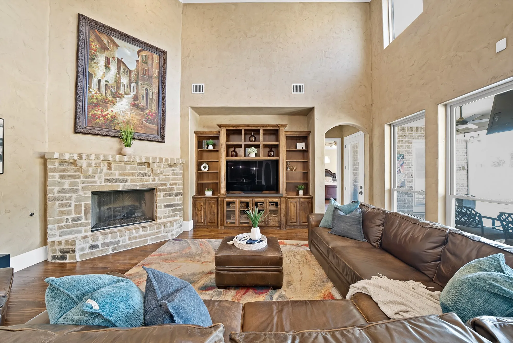Living area featuring a corner stone-finish fireplace, built-in wood cabinetry, high ceilings, large windows, and hand scraped hardwood floors