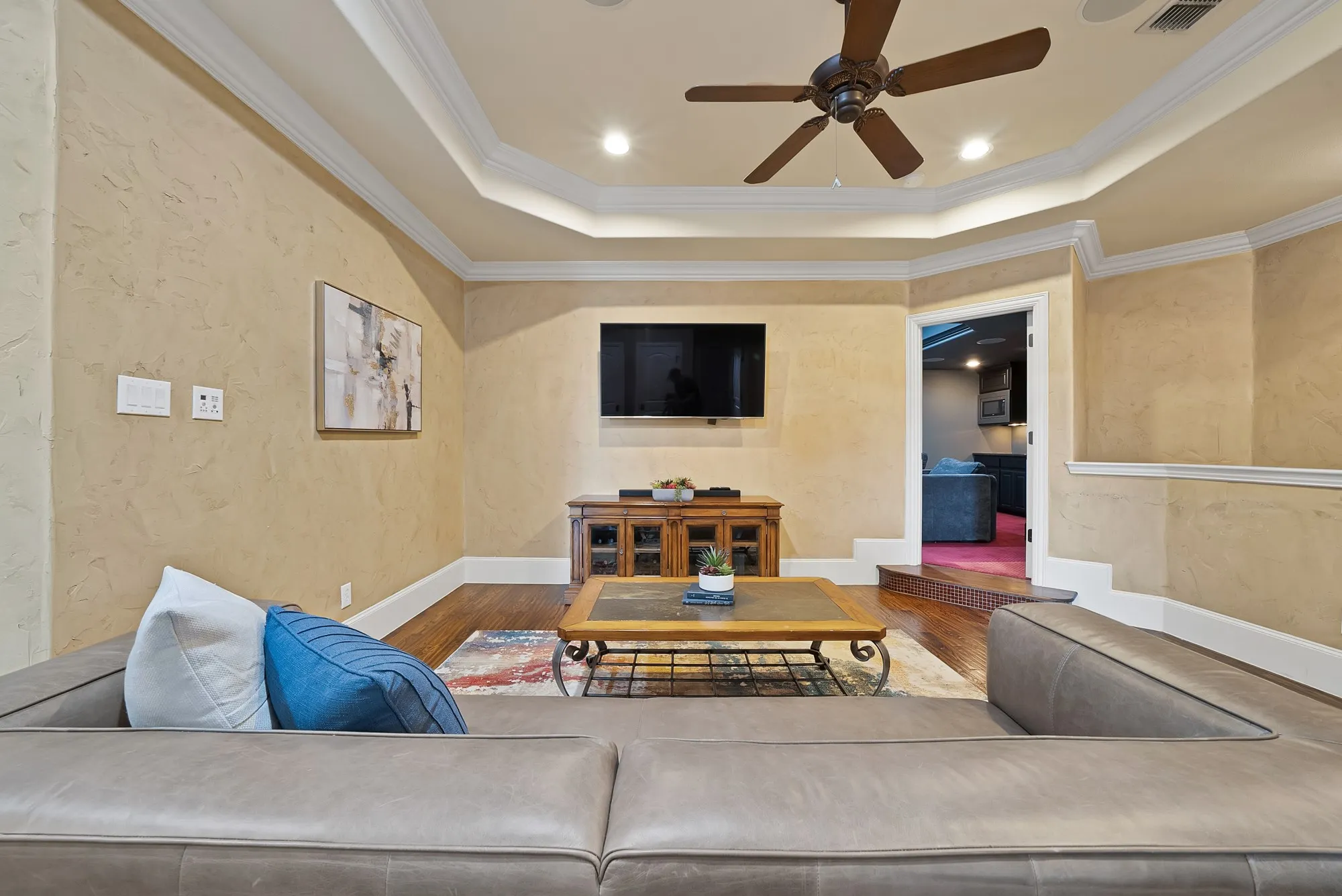 Recessed ceiling with crown molding, hand scraped hardwood floors, textured wall finish, wood media console, and a ceiling fan