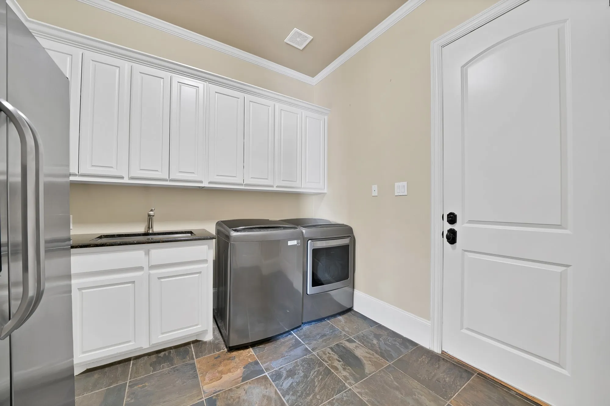 White shaker cabinetry, black countertop with undermount sink, multi-toned tile flooring, and a white paneled door with an arched top