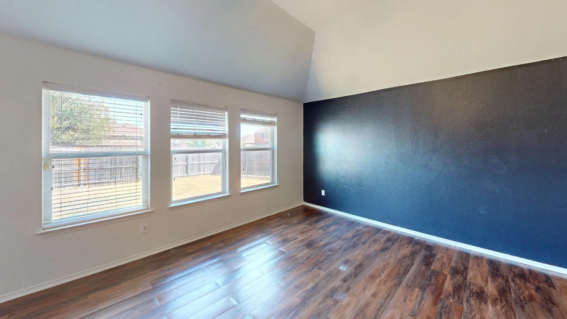 Wood-finish flooring with a dark accent wall and three windows