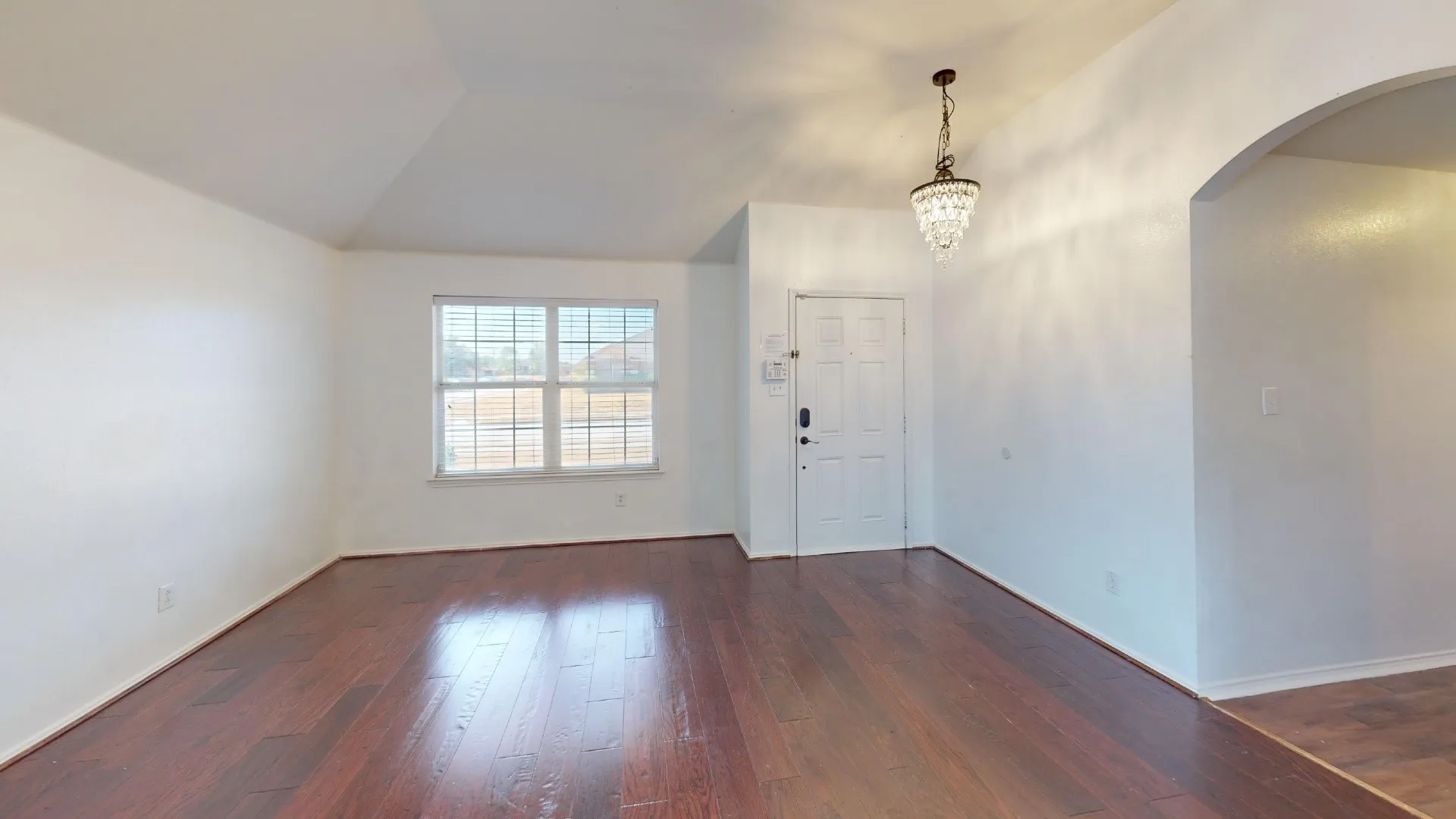 Rich wood-finish flooring, a decorative chandelier, and an arched entry