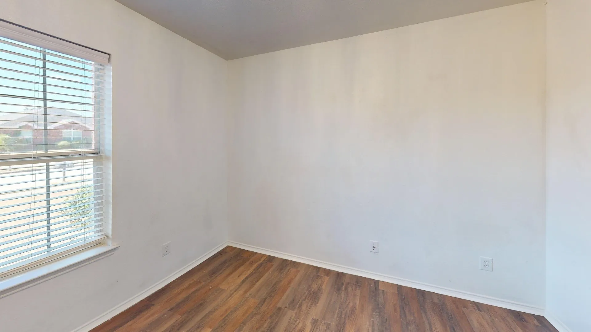 Wood-finish flooring with white baseboards, bright white walls, and a window with blinds