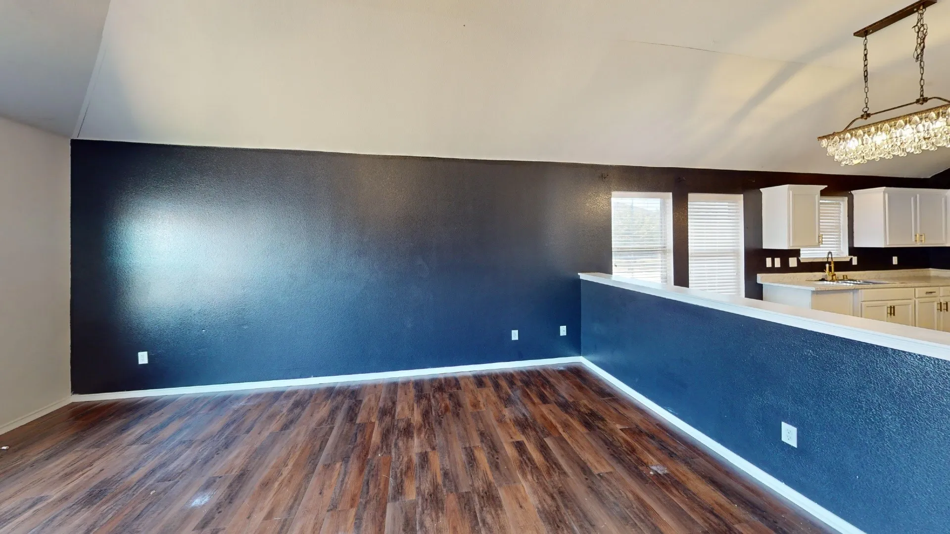 Wood-finish flooring, vaulted ceilings, kitchen with white cabinetry, light-toned countertops, and a crystal chandelier