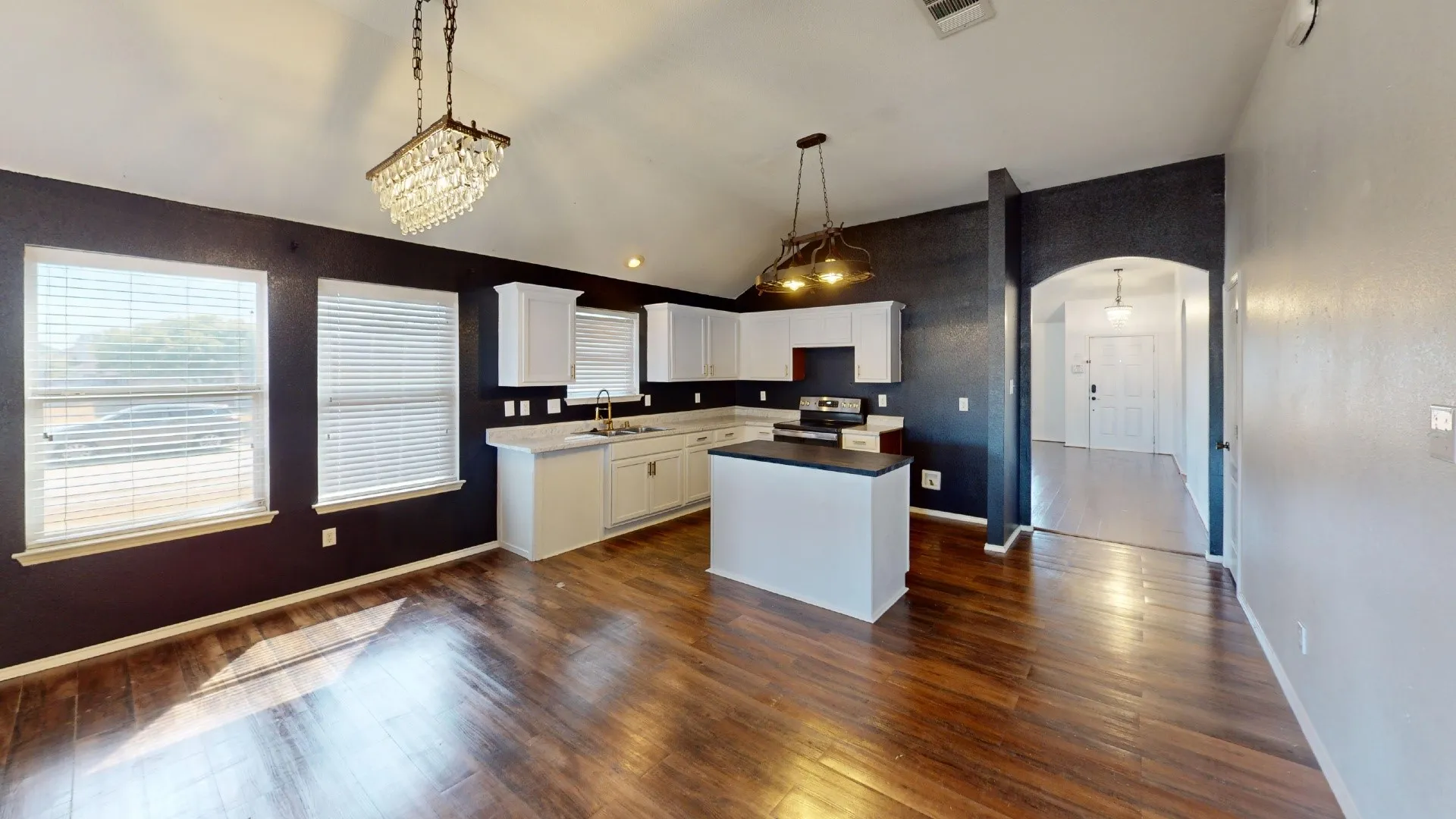 Vaulted ceiling with a crystal chandelier, wood-finish flooring, white cabinetry, kitchen island with dark countertop, and an arched entry