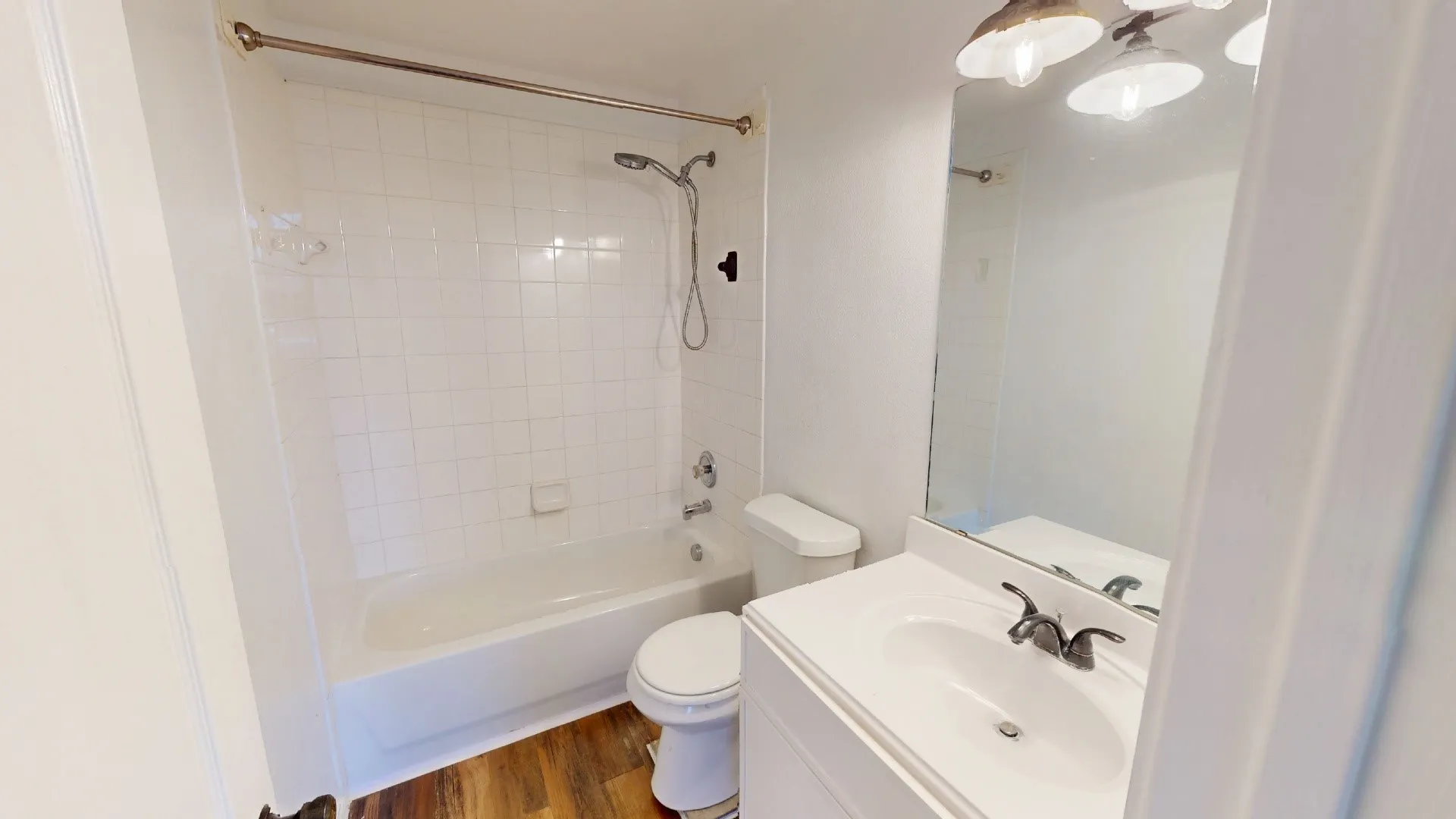 White tiled shower surround, bathtub, toilet, vanity with integrated sink, and overhead light fixture