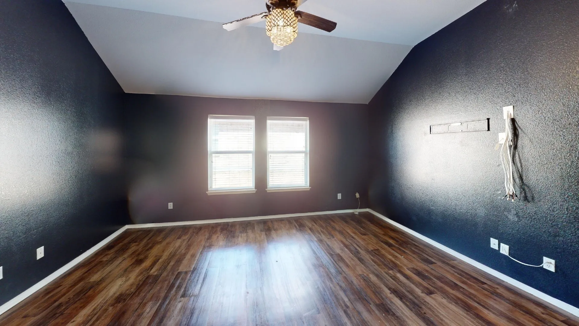 Vaulted ceiling with a decorative ceiling fan, wood-finish flooring, and two windows