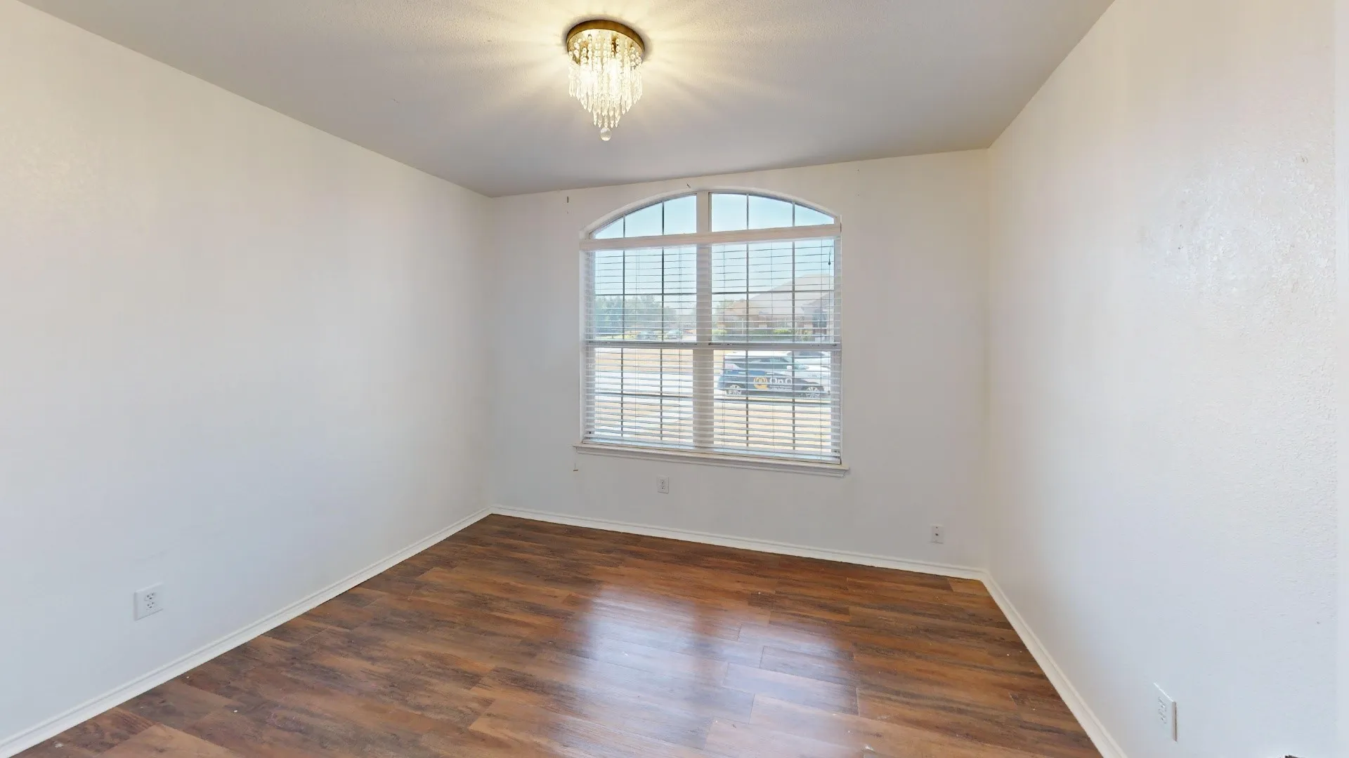 Arch-top window with horizontal blinds, wood-finish flooring, and a crystal flush mount light fixture