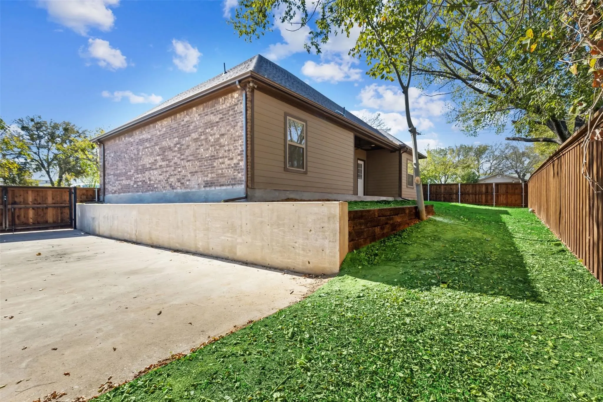 Brick and siding exterior with a dark roof, concrete retaining wall, and a wood privacy fence