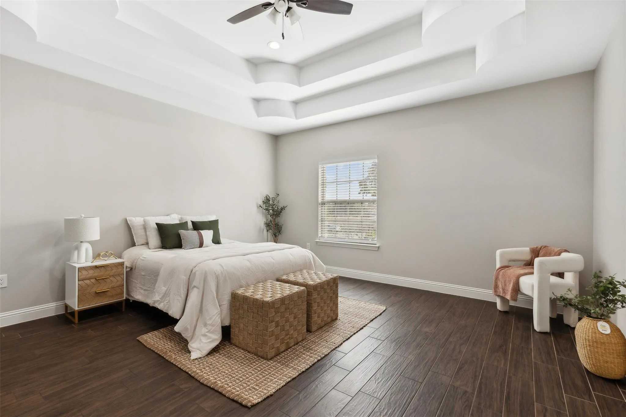 Tray ceiling with layered design, ceiling fan with integrated lighting, wood-finish flooring, and a window with blinds