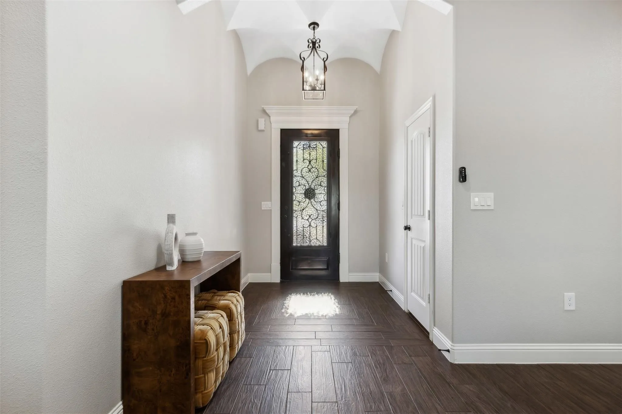 Vaulted ceiling with decorative chandelier, dark wood-finish flooring, white trim, and a frosted glass-paneled entry door