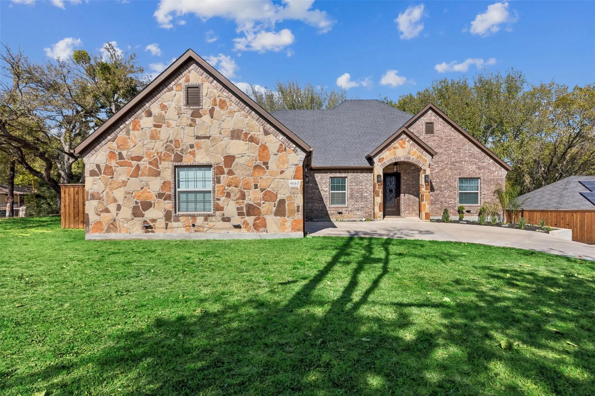 Stone and brick exterior with a dark shingle roof, arched entry, and a paved driveway