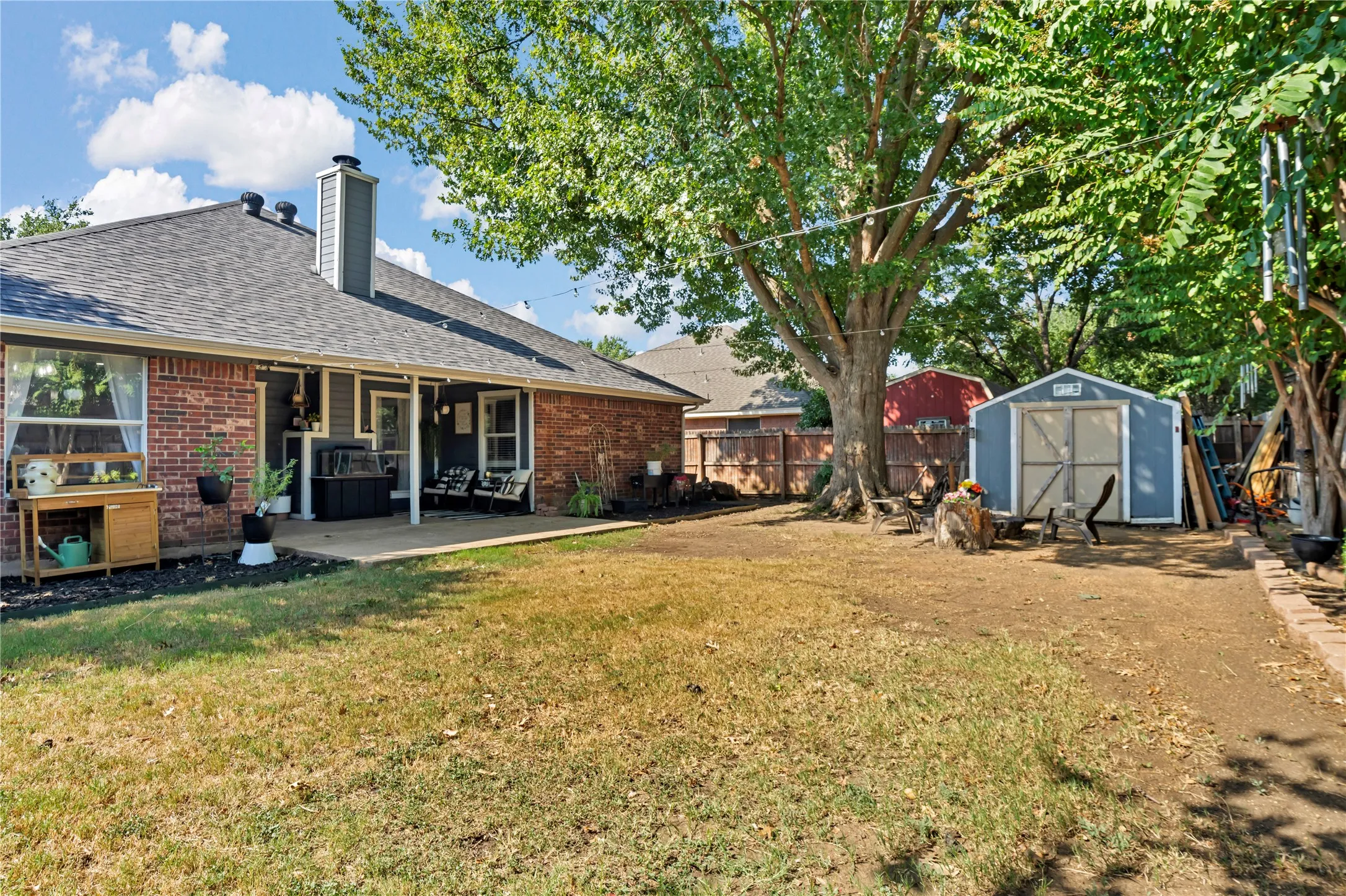 Brick exterior with a covered patio, featuring a dark shingle roof and a detached shed