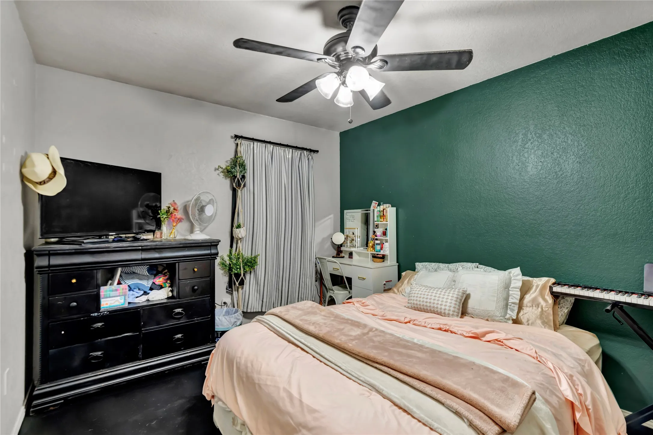 Ceiling fan with integrated lighting, textured accent wall, window with drapery, and dark flooring