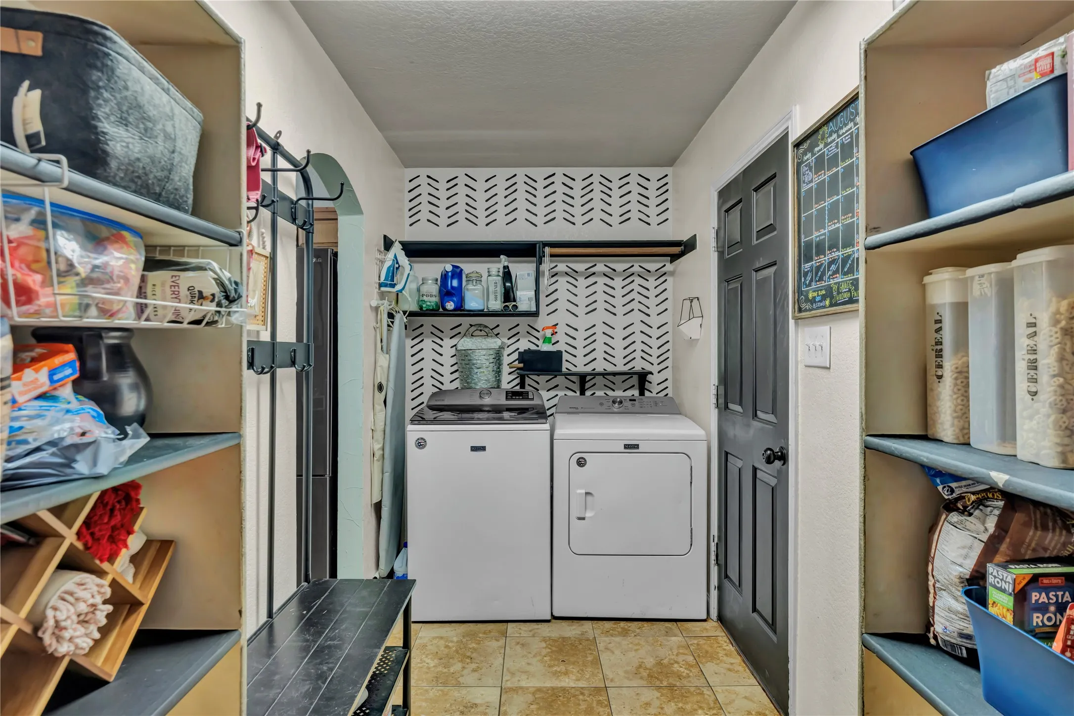Laundry area with patterned accent wall, built-in shelving, and tiled flooring