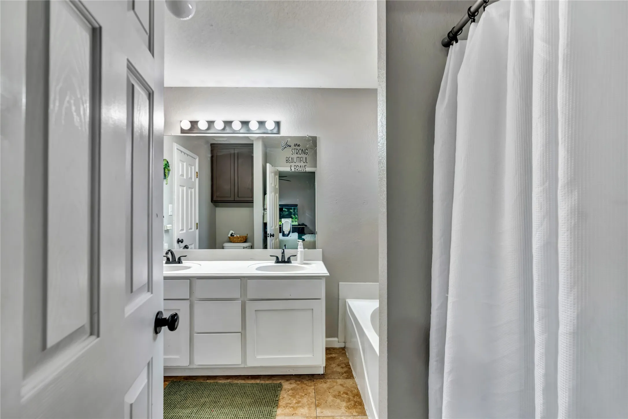 Double vanity with white cabinetry and integrated sinks, large vanity mirror, and overhead vanity lighting