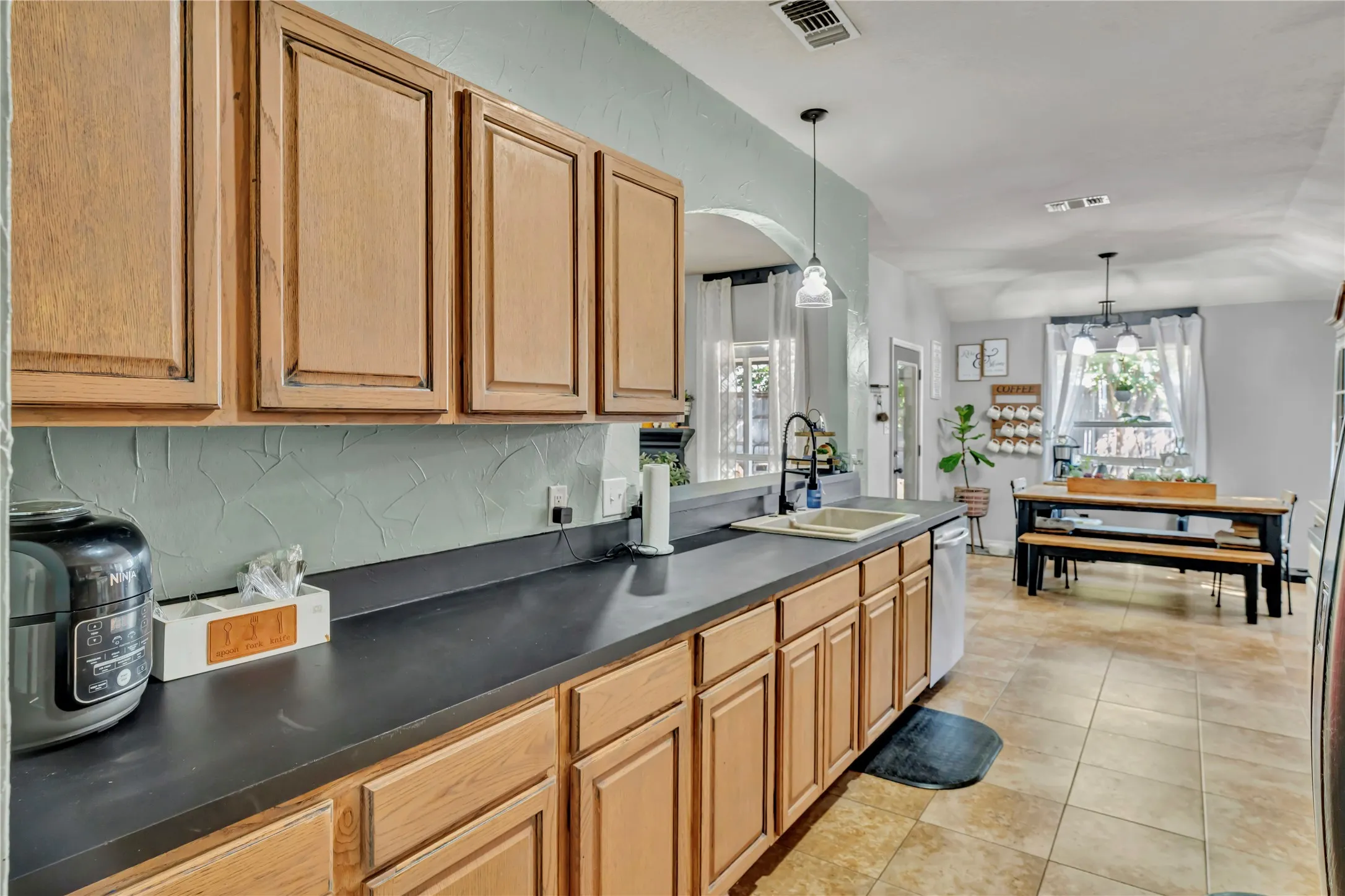 Kitchen featuring wood cabinetry, dark countertops, a stainless steel sink with a black faucet, and tile flooring