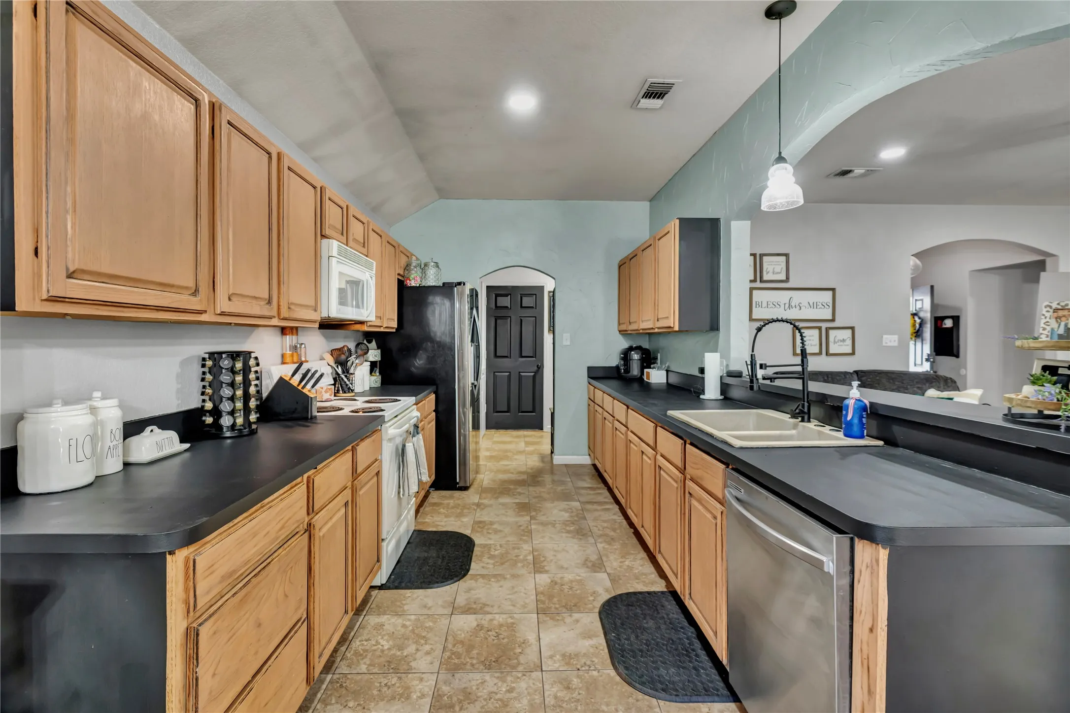 Galley kitchen featuring wood-finish cabinetry, dark countertops, tile flooring, and integrated stainless steel appliances