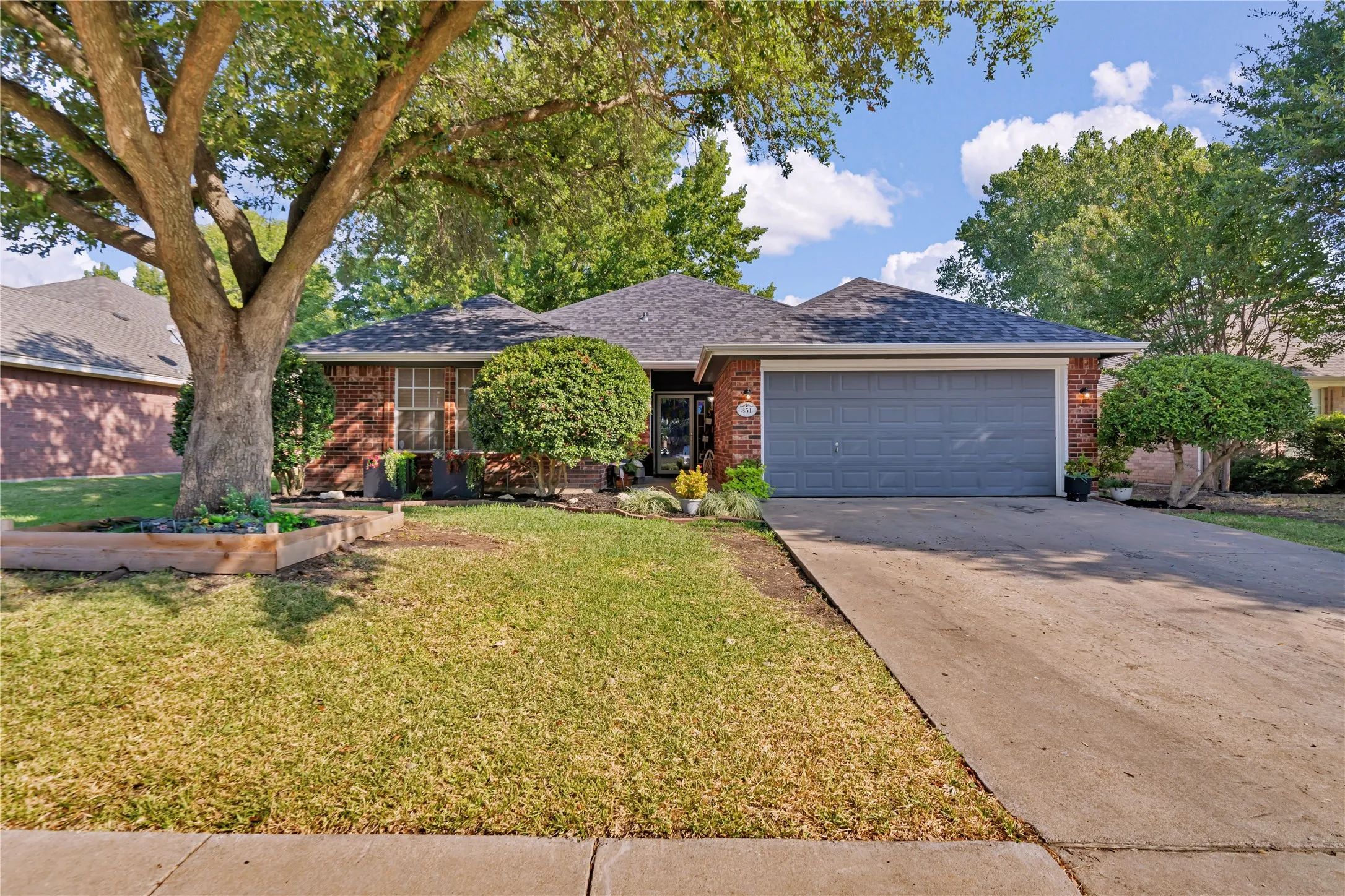 Brick exterior with a dark-toned roof, attached garage with a panel door, concrete driveway, and mature landscaping