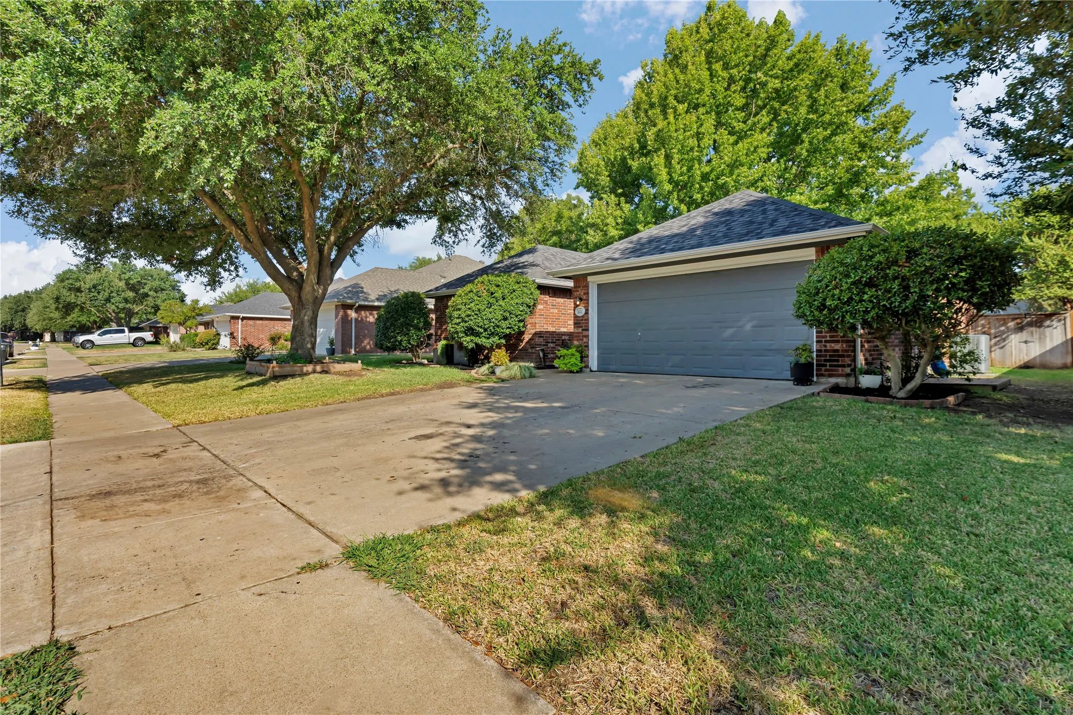 Brick exterior with a gray garage door, concrete driveway, and mature landscaping